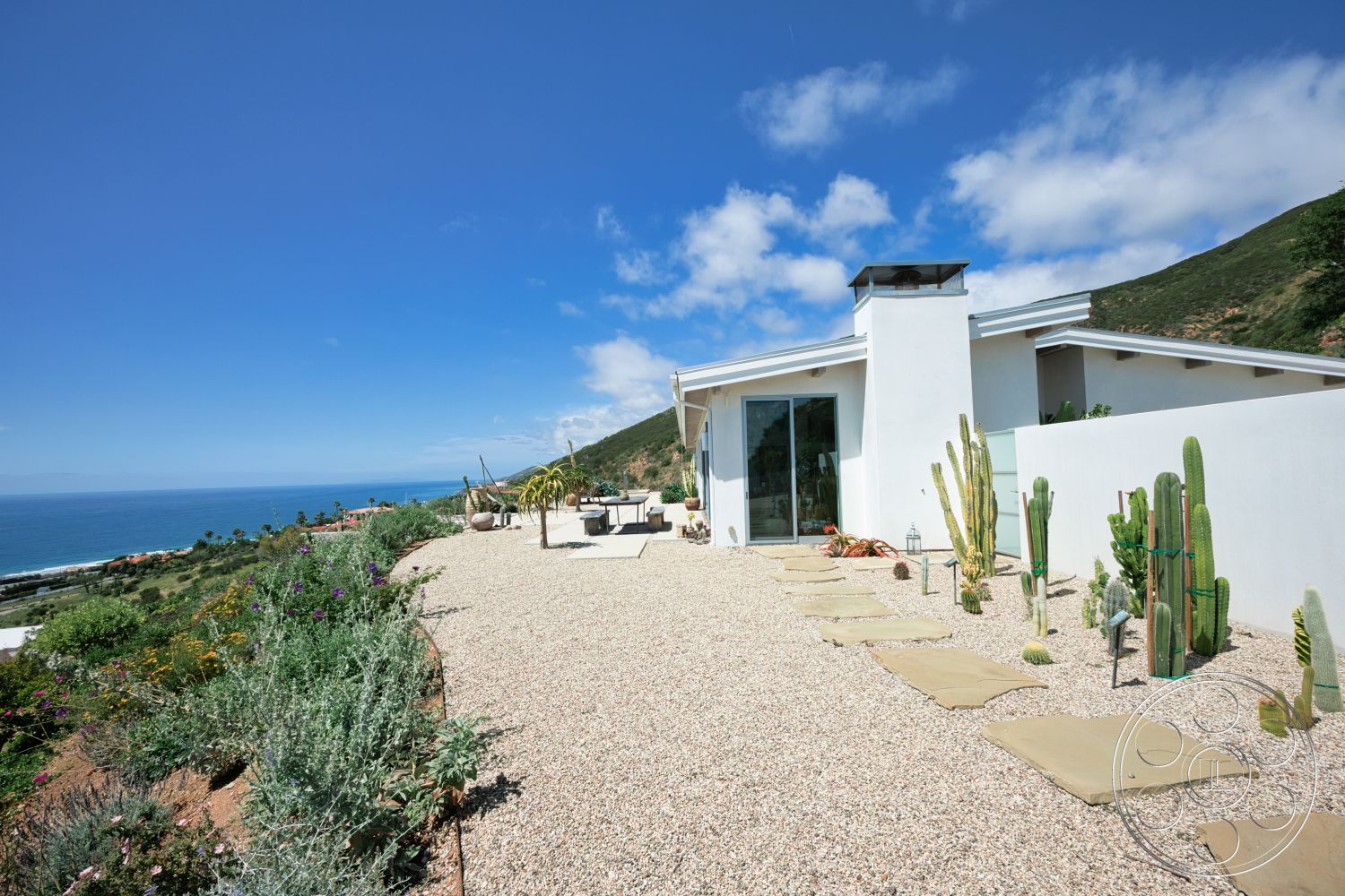 Modern 523 - exterior, white stucco walls, sliding glass doors, gravel landscaping, ocean view, patio seating area, modern home, desert plants, hillside location, cacti garden, flat roof design, flagstone stepping stones
