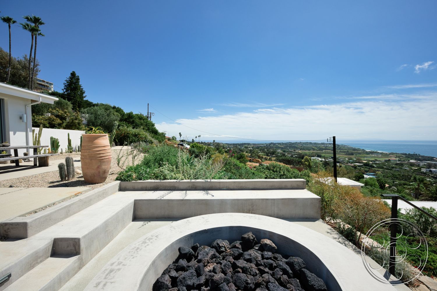Modern 523 - exterior, vegetation, minimalist design, wooden dining table, concrete steps, modern architectural style, desert landscaping, outdoor living area, natural stone planters, scenic hillside location, view of ocean, round fire pit with lava rocks, curved concrete seating