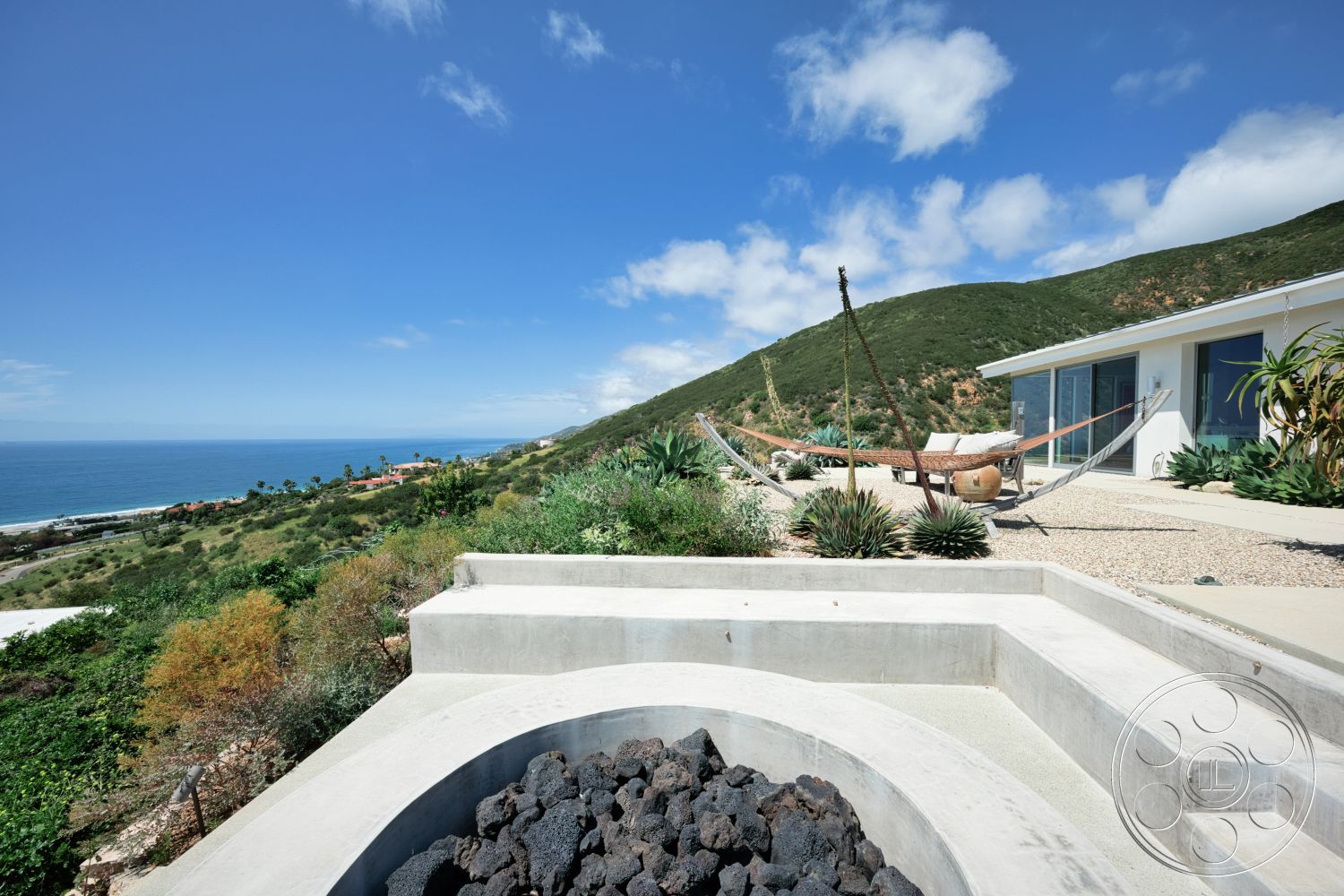 Modern 523 - exterior, large glass windows, modern architectural style, white siding, ocean view, hillside location, concrete seating area, open patio area, landscaped garden with succulents, curved concrete fire pit, wooden hammock