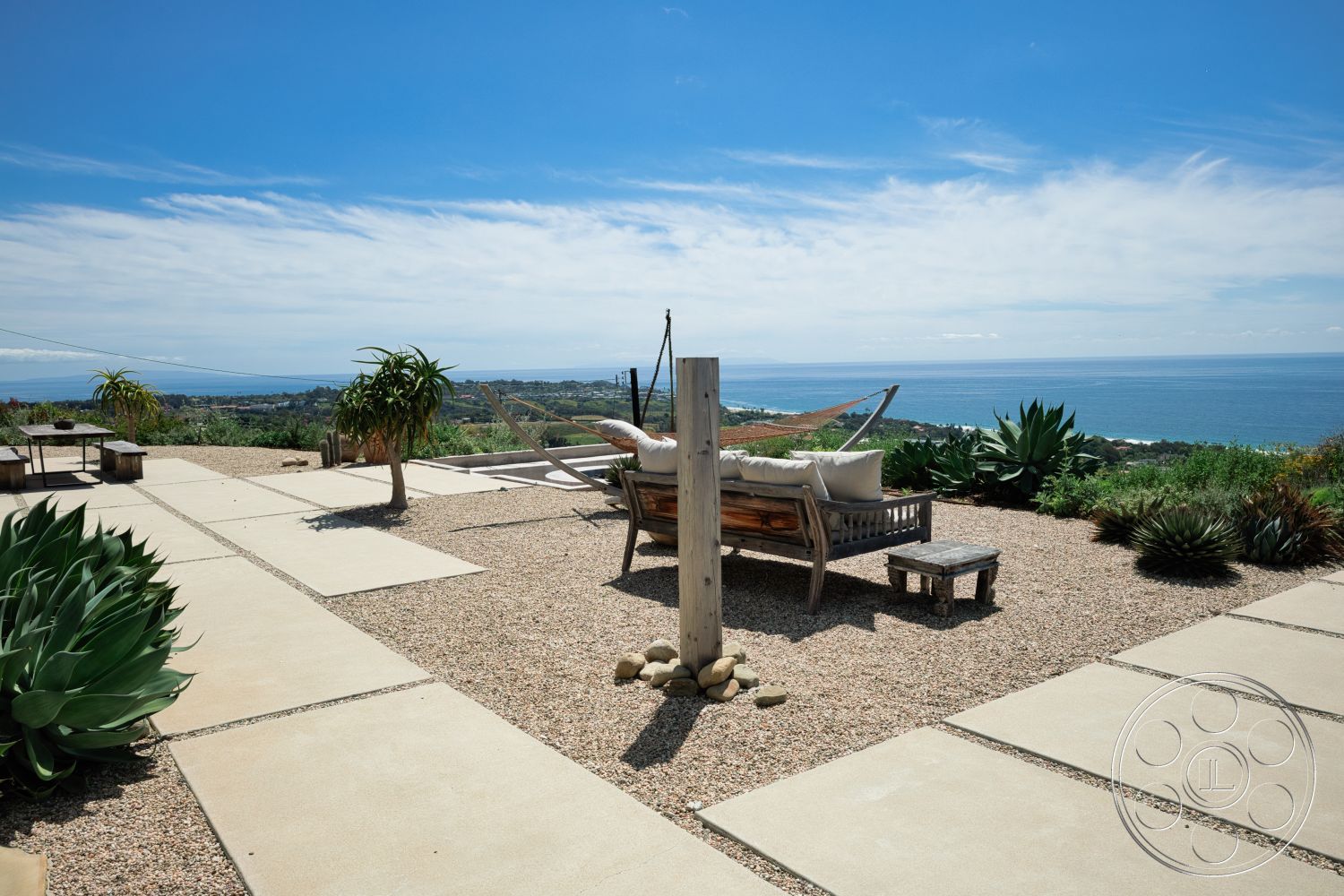 Modern 523 - exterior, minimalist design, gravel landscaping, open outdoor space, landscaped hillside, succulent plants, wooden lounge chair, panoramic ocean view, concrete patio flooring, modern outdoor seating area, slip-resistant surface, rustic wooden post, recreational patio area