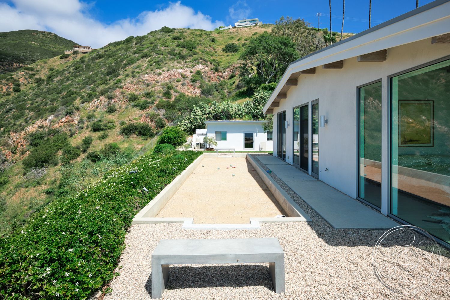 Modern 523 - exterior, white stucco walls, large glass sliding doors, concrete bench, gravel patio flooring, concrete pool border, surrounding hillside view, wood beam overhang, flat-roofed modern house, linear pool design