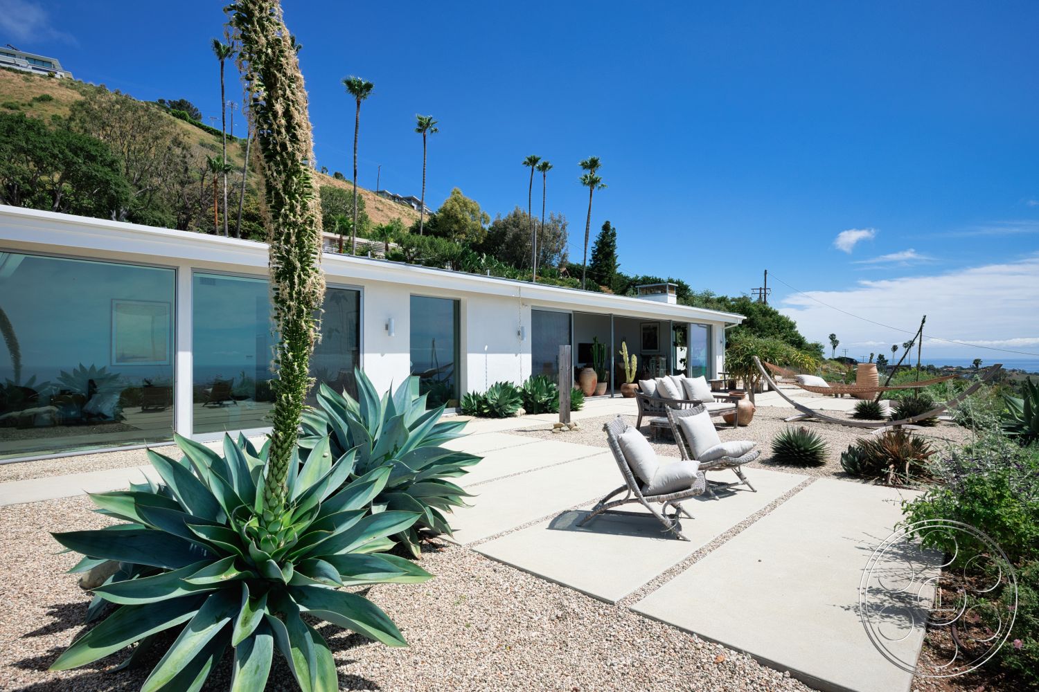 Modern 523 - exterior, modern architecture, glass sliding doors, mountain backdrop, flat roof design, concrete patio flooring, palm tree accents, rectangular concrete slabs, ocean view setting, landscape with succulents, gravel garden, hammock seating area
