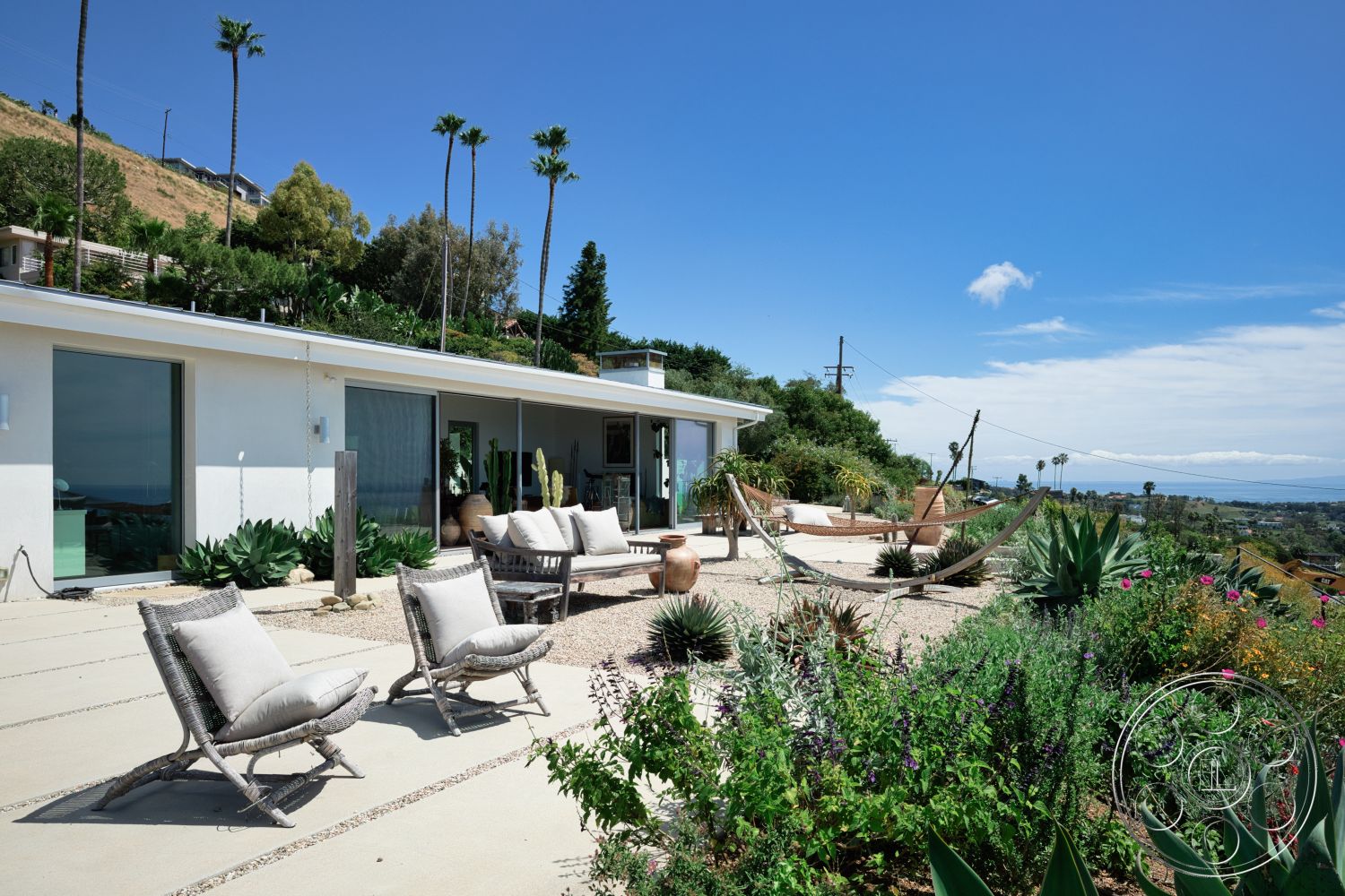 Modern 523 - exterior, glass sliding doors, mountain view, desert landscaping, tropical palm trees, succulent garden, wooden lounge chairs, outdoor living area, hammock, hilltop location, concrete patio flooring, woven patio chairs, modern white stucco walls