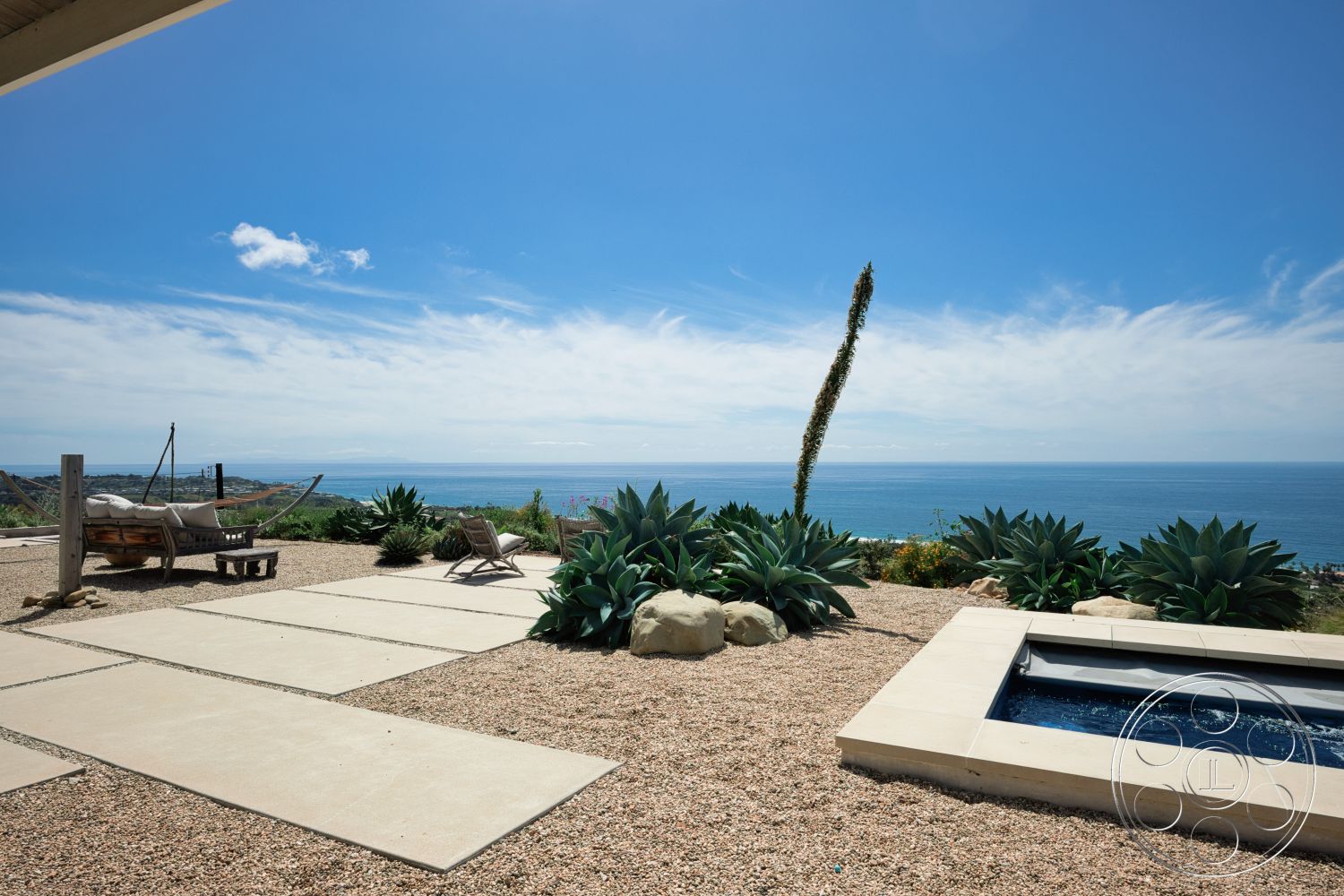 Modern 523 - exterior, natural stone accents, gravel landscaping, wooden lounge chairs, spa hot tub, concrete patio flooring, rectangular concrete patio, ocean view setting, sunny coastal environment, large outdoor plants, hammock stand
