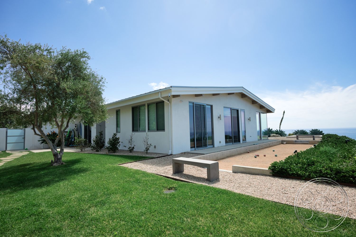 Modern 523 - exterior, low-maintenance landscaping, modern architecture, floor-to-ceiling windows, green lawn, single-story home, gravel landscaping, stucco walls, concrete patio border, flat roof with overhang, wooden beam accents, desert coastal setting