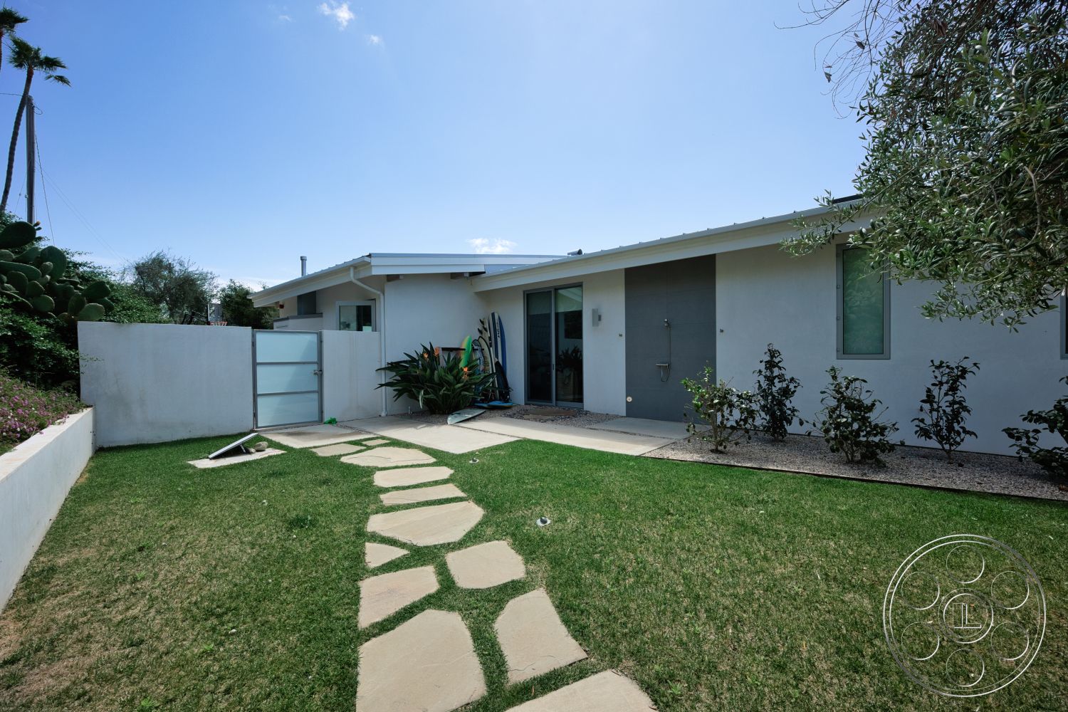 Modern 523 - exterior, minimalist design, stone pathway, lush landscaping, glass entry door, green grass lawn, rectangular windows, modern house, stucco exterior walls, concrete patio area, flat roofline, desert garden setting, concrete low fencing