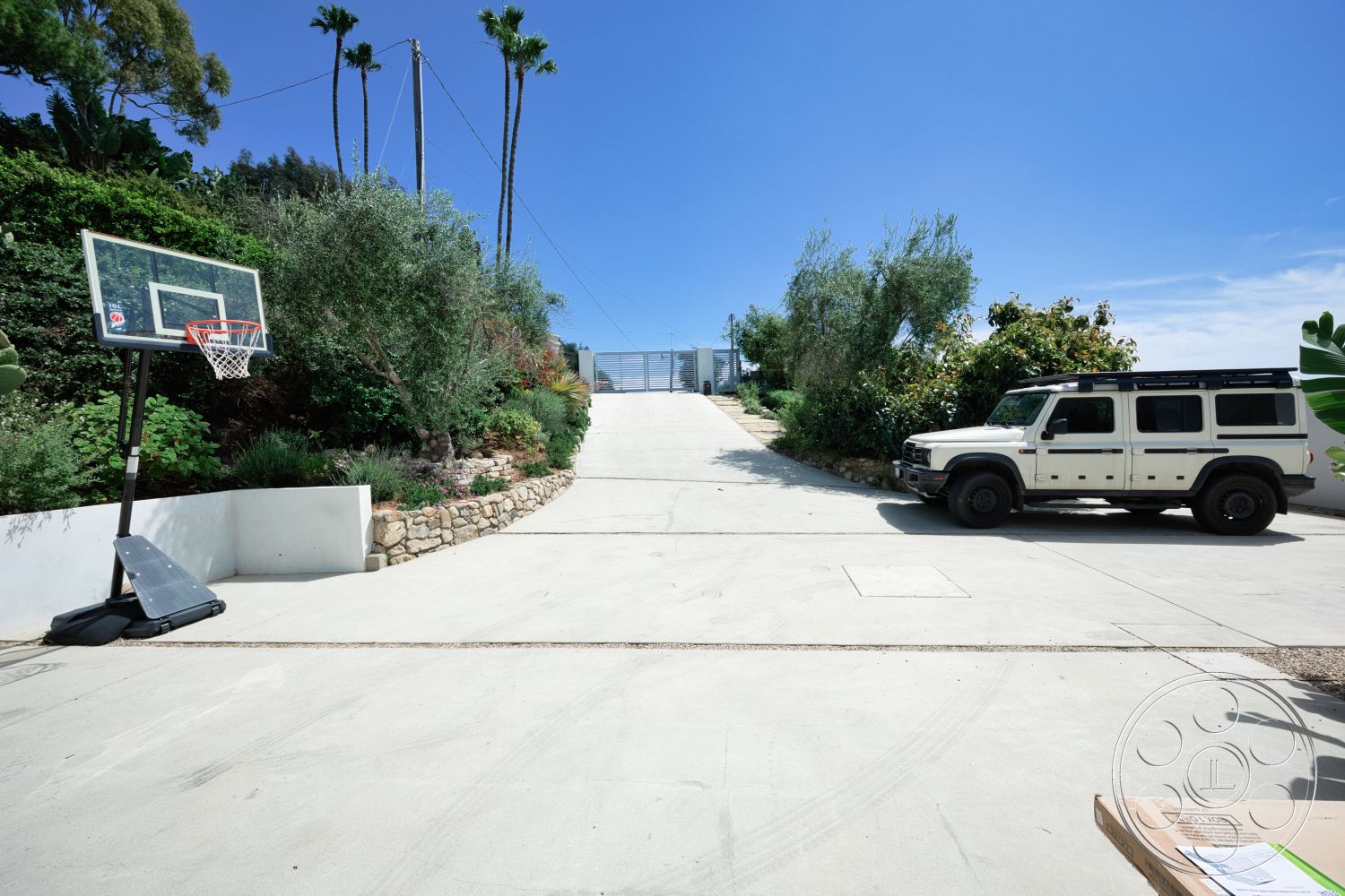 Modern 523 - exterior, vegetation, palm trees, basketball hoop, concrete driveway, natural stone retaining wall, hilltop location, landscaped garden area, gravel border landscaping, white painted wall, steep driveway incline