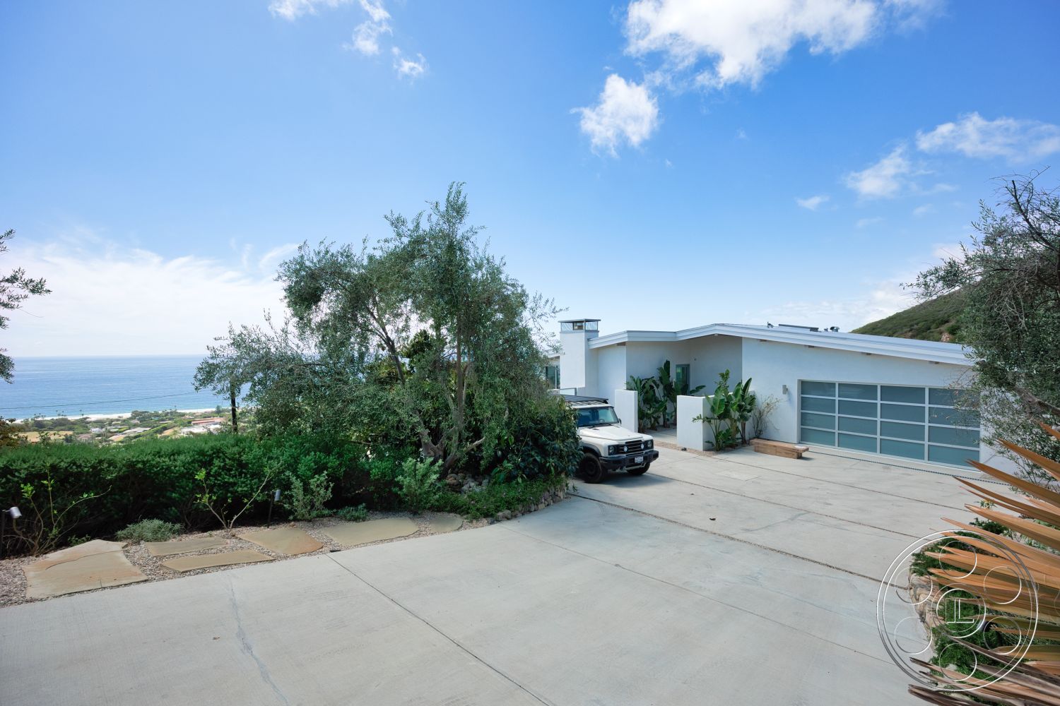 Modern 523 - exterior, flat roof, wooden deck, city skyline view, concrete driveway, glass garage door, stucco walls, landscape greenery, oceanfront property