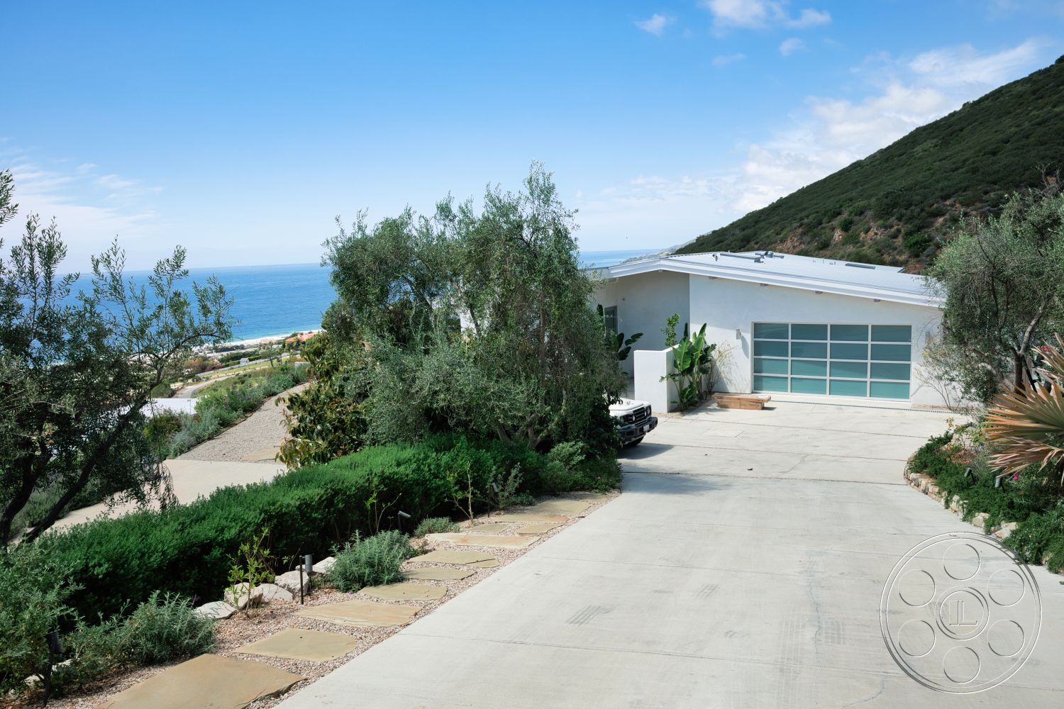 Modern 523 - exterior, modern architectural style, concrete driveway, natural stone pathway, hillside location, large glass garage door, flat roof design, rectangular driveway, white stucco exterior walls, landscaped garden with shrubs, ocean view setting