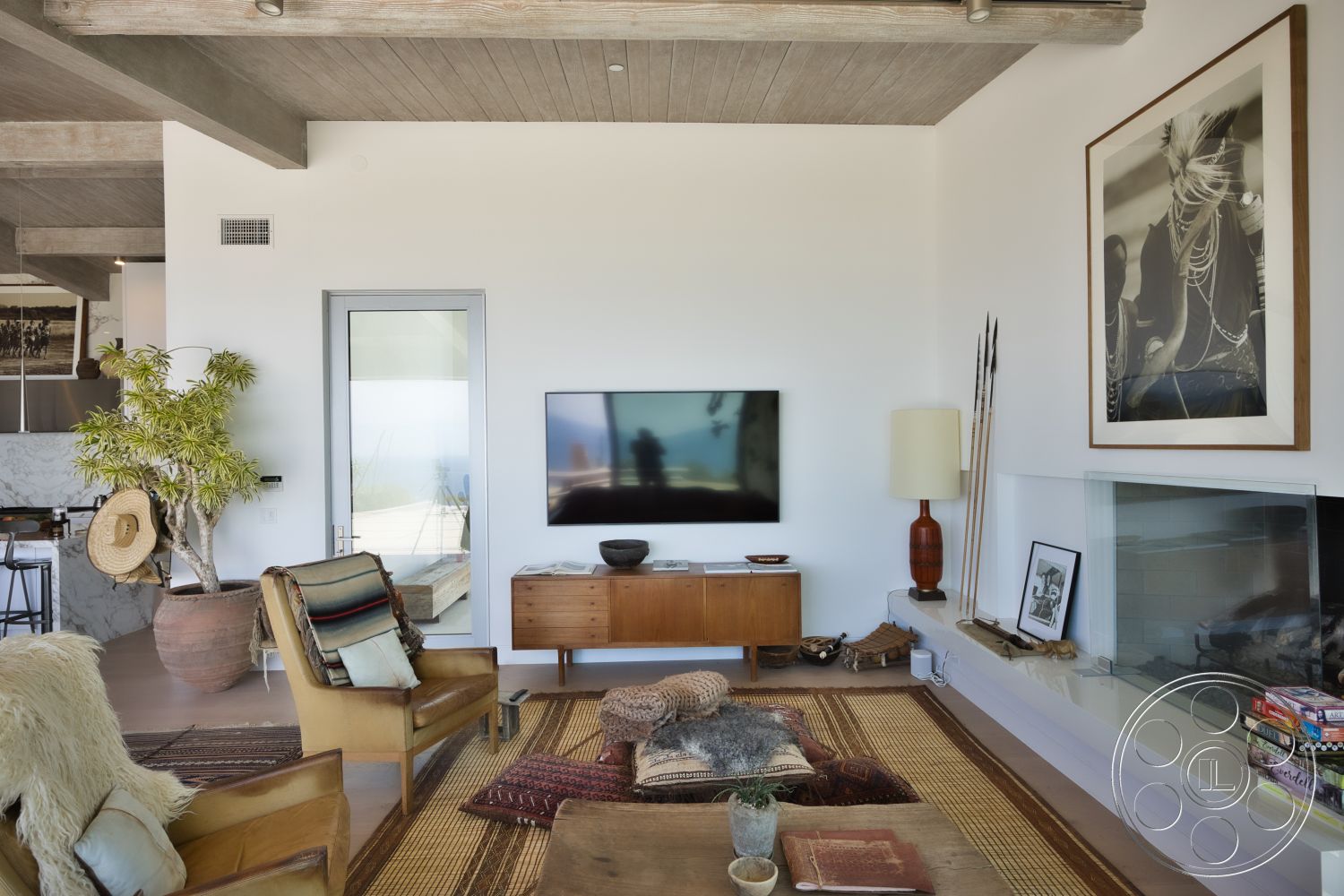 Modern 523 - textured area rug, polished concrete flooring, mid-century modern furniture, glass sliding door, exposed wood ceiling beams, natural light interior, white painted walls, open concept living area, stone fireplace wall, indoor potted plant, modern wooden media console, art gallery wall with framed photos