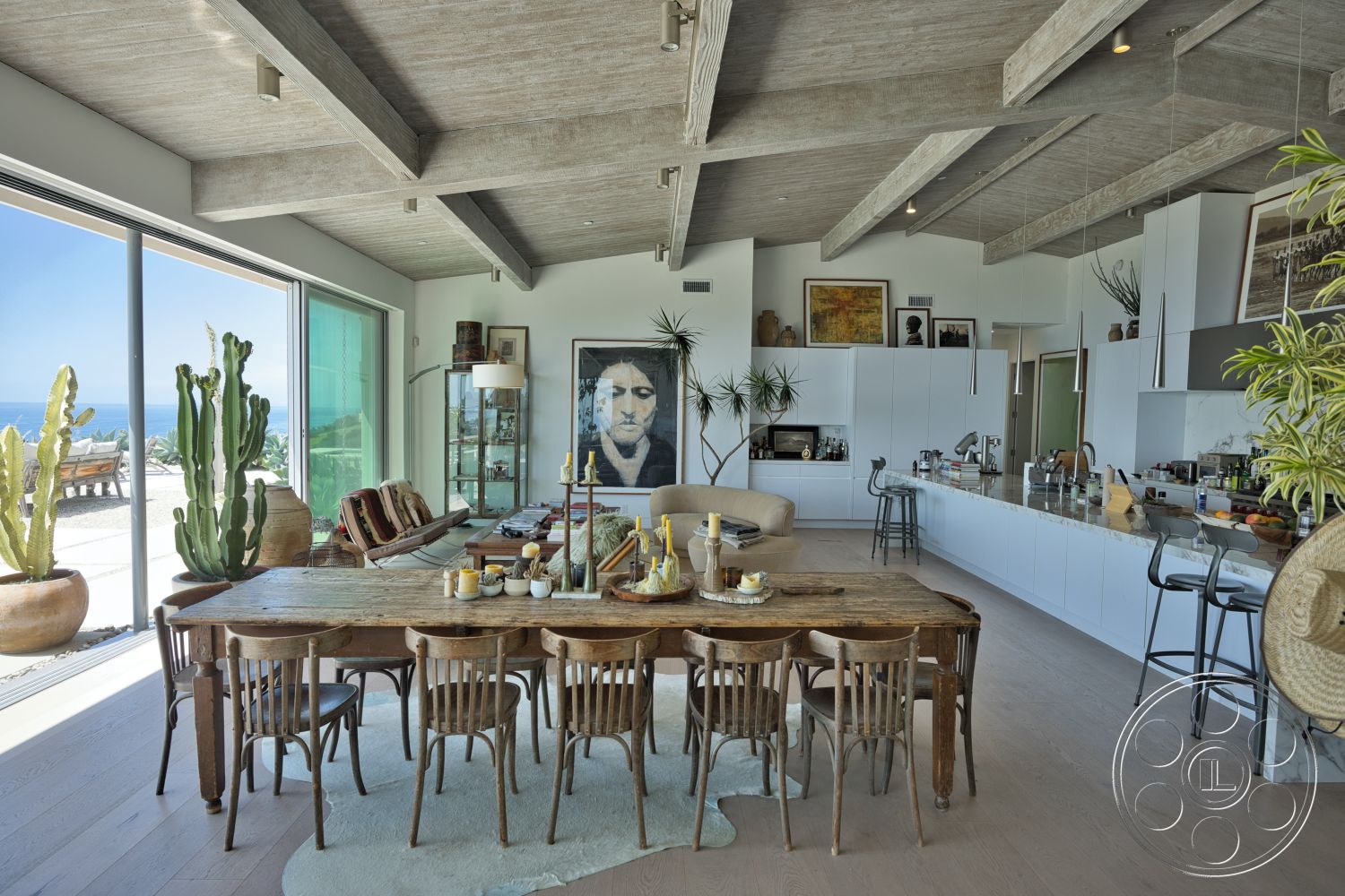 Modern 523 - neutral color palette, light hardwood flooring, modern art wall decor, large floor-to-ceiling windows, rectangular dining table, exposed wood ceiling beams, concrete kitchen countertop, potted indoor plants, open-plan interior, white flat-panel kitchen cabinets, rustic wooden dining chairs, beachfront view setting