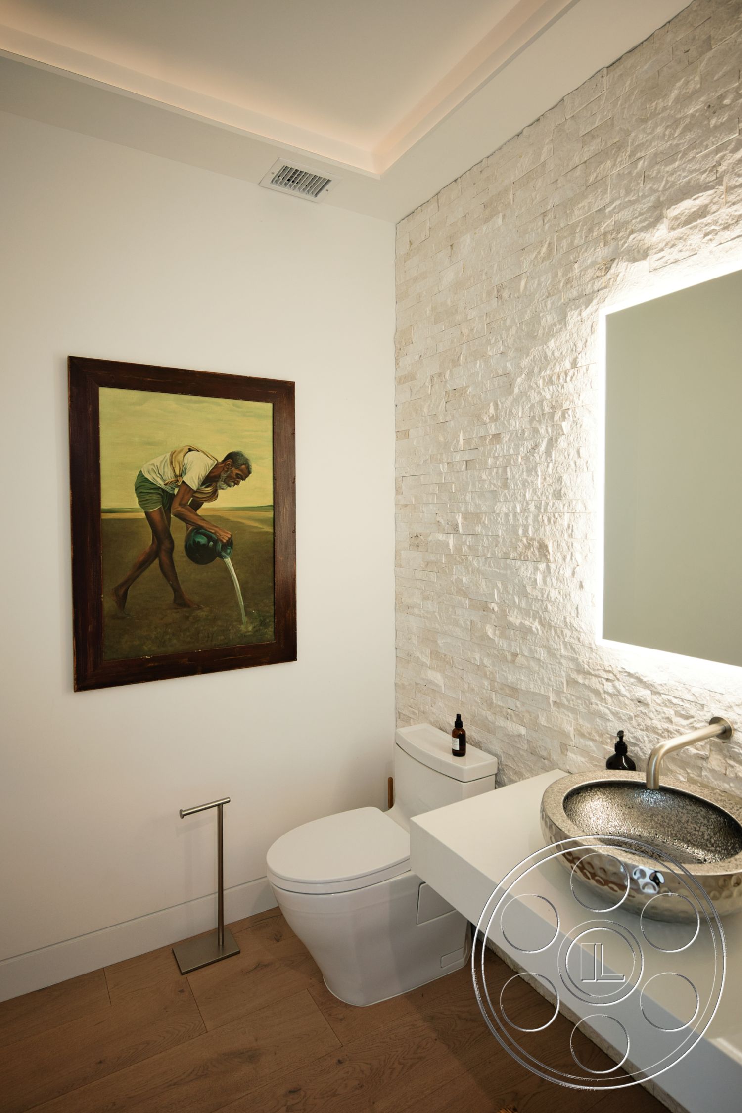 Modern 523 - minimalist aesthetic, framed artwork, backlit mirror, white painted walls, textured stone feature wall, wall-mounted toilet, wooden bathroom flooring, round metallic vessel sink, modern bathroom faucet