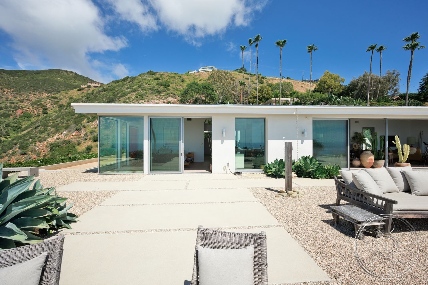Modern 523 - exterior, large glass sliding doors, concrete patio flooring, minimalist outdoor furniture, sunny outdoor environment, panoramic hillside view, landscaped hillside setting, flat roof architectural style, textured gravel ground, modern square patio design, desert plants surrounding patio