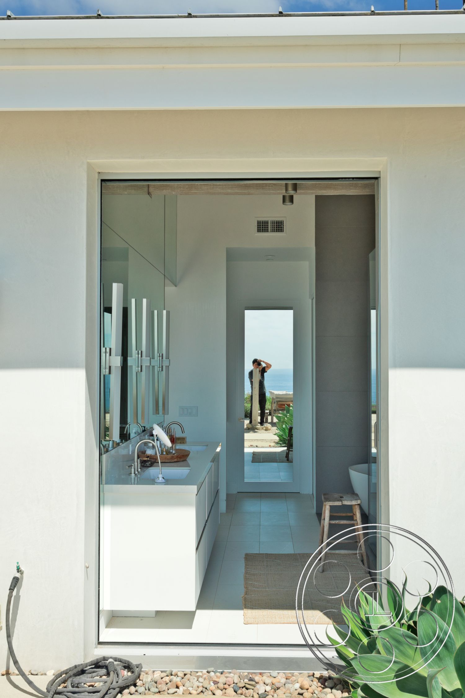 Modern 523 - minimalist decor, neutral color palette, textured area rug, floating vanity, ceramic tile flooring, well-lit space, glass bathroom mirrors, contemporary bathroom design, white painted walls, rectangular bathroom layout, open doorway to outdoor space, white vanity with sink, natural light through sliding glass doors, subtle landscaping visible through doorway
