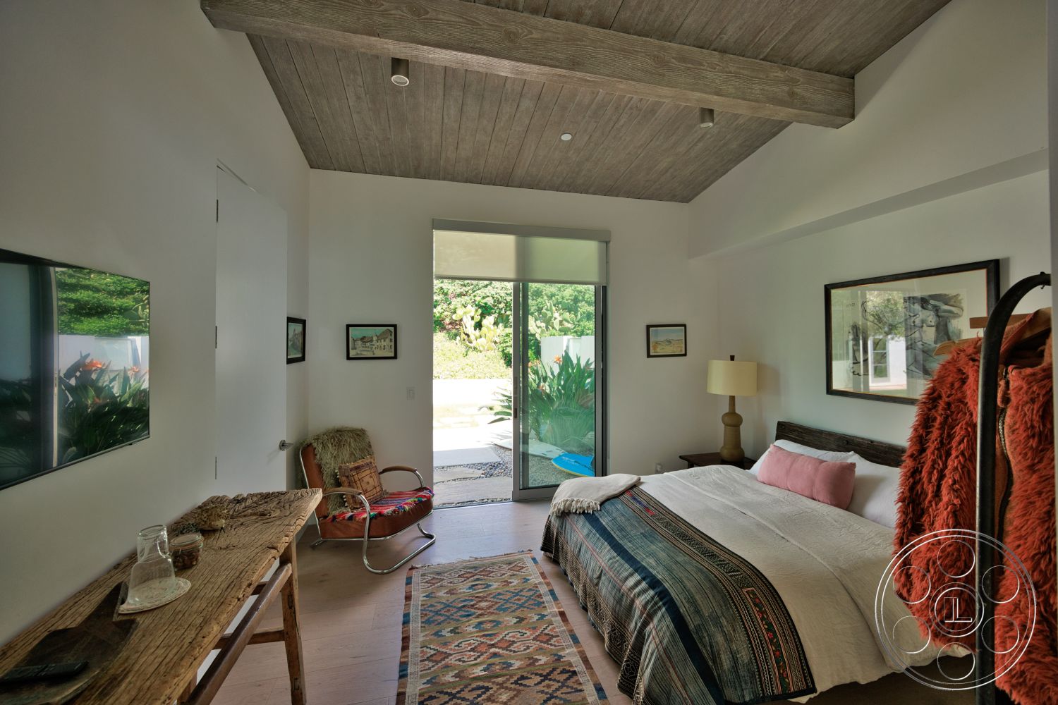 Modern 523 - minimalist decor, decorative area rug, exterior, floor-to-ceiling windows, lush garden view, contemporary lighting fixture, modern lounge chair, hardwood bedroom floors, wood beam ceiling, white painted walls, modern bed with decorative blanket, rustic wooden nightstand, geometric patterned throw blanket