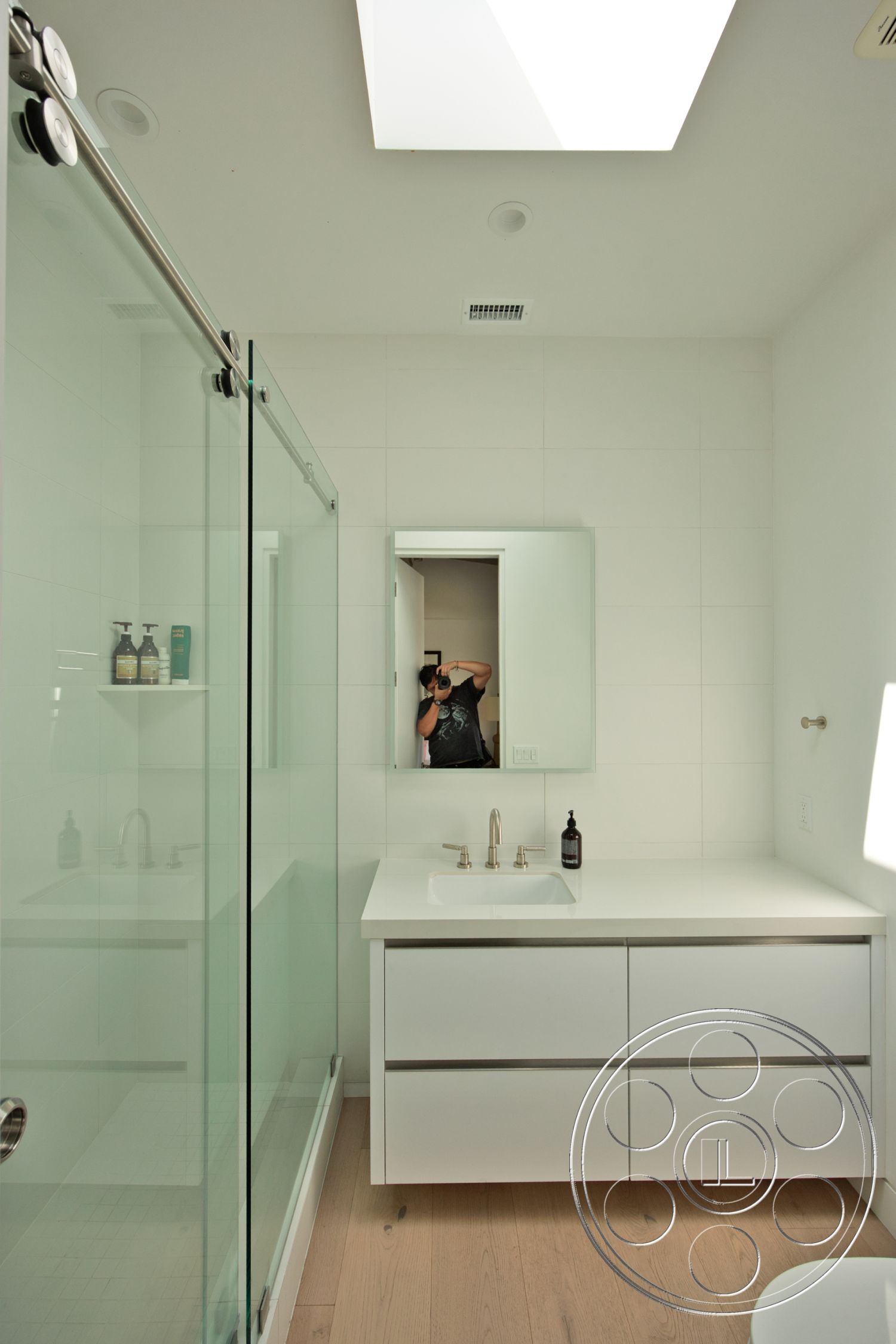 Modern 523 - glass shower doors, minimalist bathroom design, skylight ceiling, light wood plank flooring, large rectangular mirror, brushed nickel faucet, modern floating vanity, concrete shower floor, white tile bathroom walls