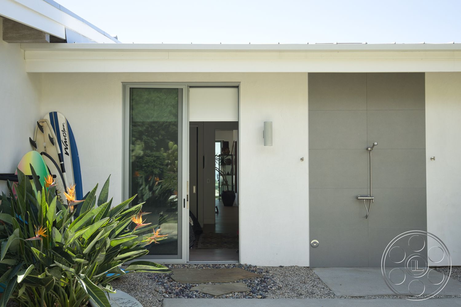 Modern 523 - exterior, white stucco walls, modern architecture, sliding glass doors, tropical landscaping, angled roofline, gray stone feature wall, beach house entryway, decorative pebbled walkway, surfer aesthetic