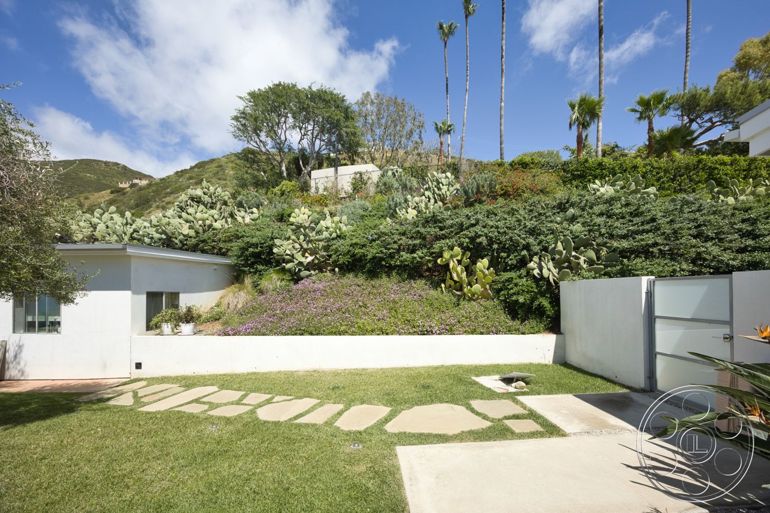 Modern 523 - exterior, white stucco walls, concrete pathway, mountain view, colorful flowering plants, tropical palm trees, hilltop location, landscaped garden beds, flagstone stepping stones, lawn grass area, native plants and cacti, concrete fence, modern glass gate