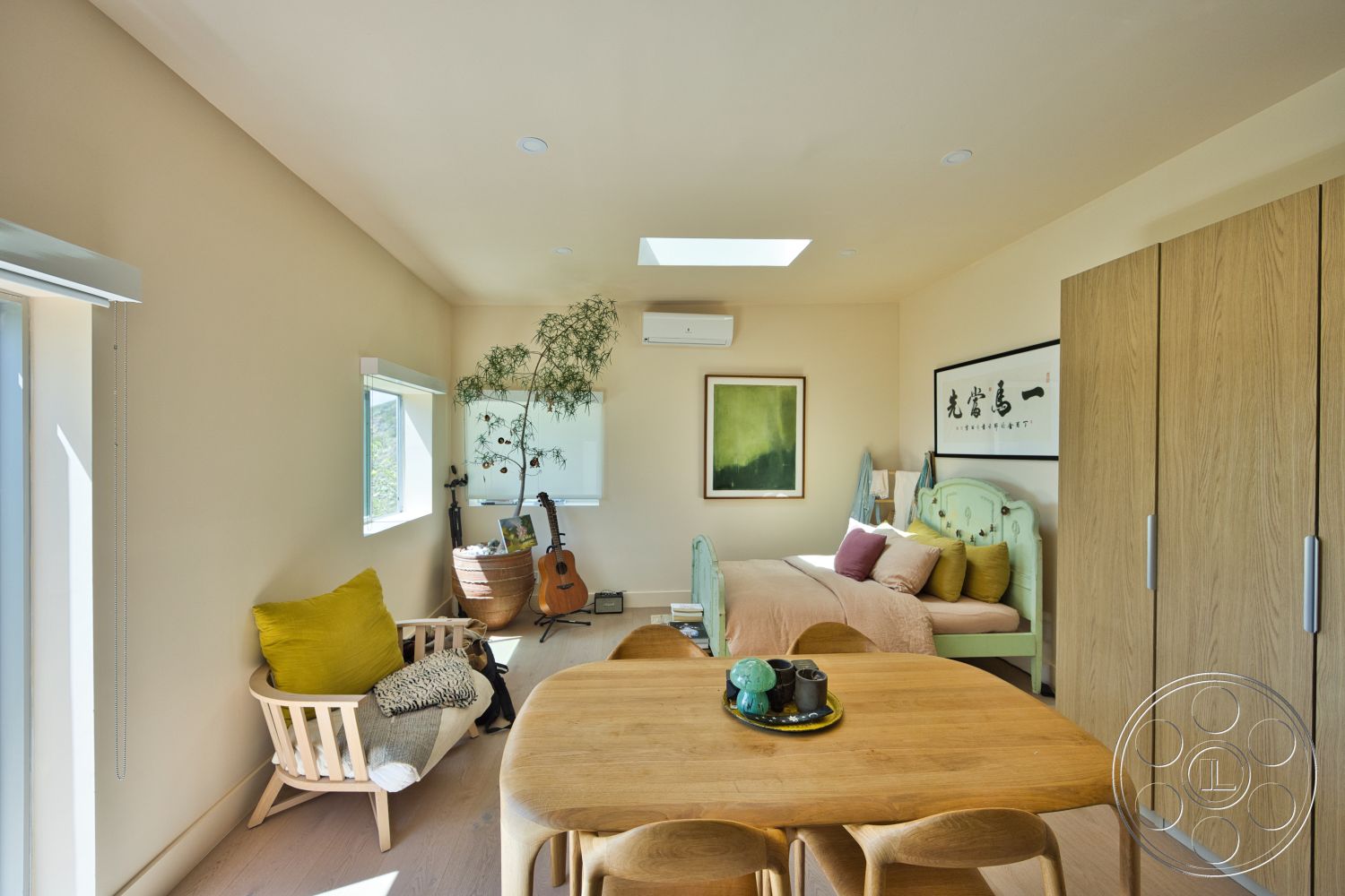Modern 523 - neutral color palette, natural light, indoor plant, light wood flooring, guitar, decorative wall art, round dining table, white painted walls, vaulted ceiling with skylight, mid-century modern chair, green upholstered bed, wooden wardrobe cabinet