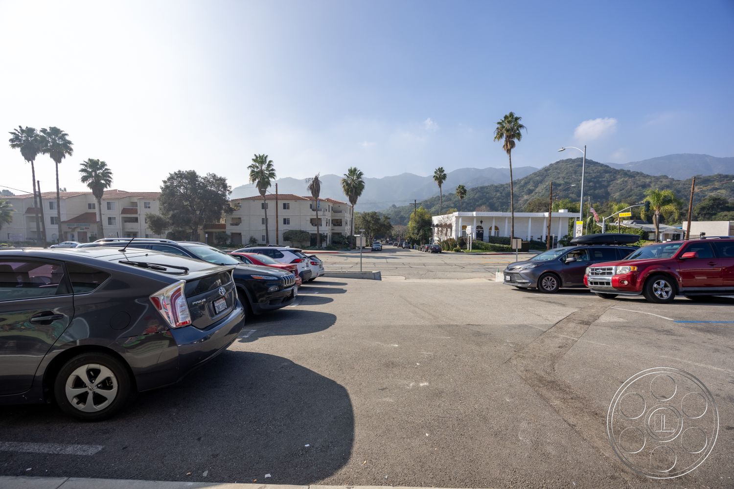 Laundromat 1 - exterior, white stucco walls, clear sky, asphalt surface, urban setting, mountain backdrop, terracotta roof tiles, paved parking lot, landscaped palm trees, multi-unit residential buildings, two-story apartment complex