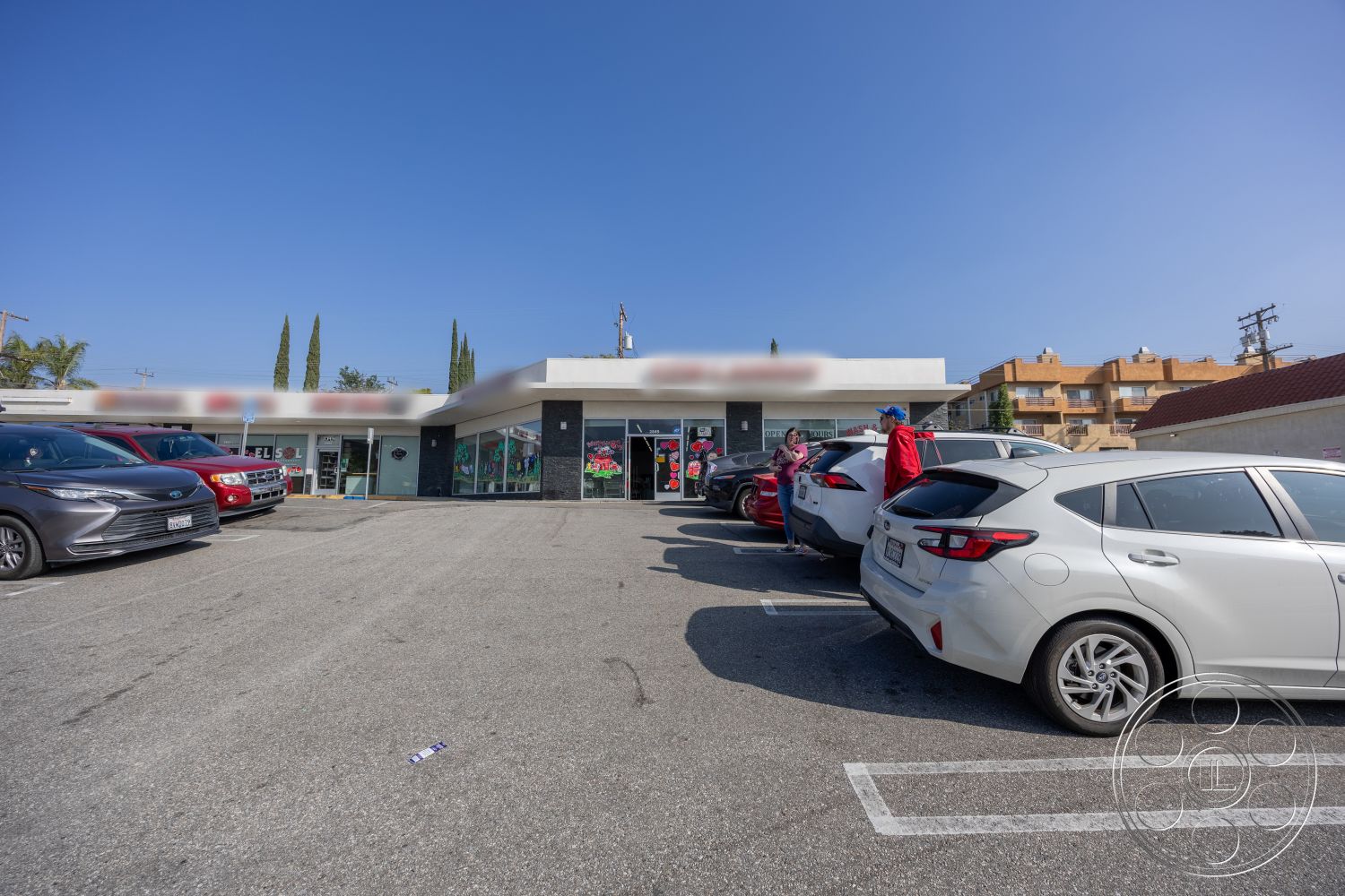 Laundromat 1 - exterior, concrete parking lot, black stone accent wall, flat roof design, stucco wall finish, glass storefront windows, urban commercial setting, paving strip parking spaces, cypress trees landscaping, single-story retail building