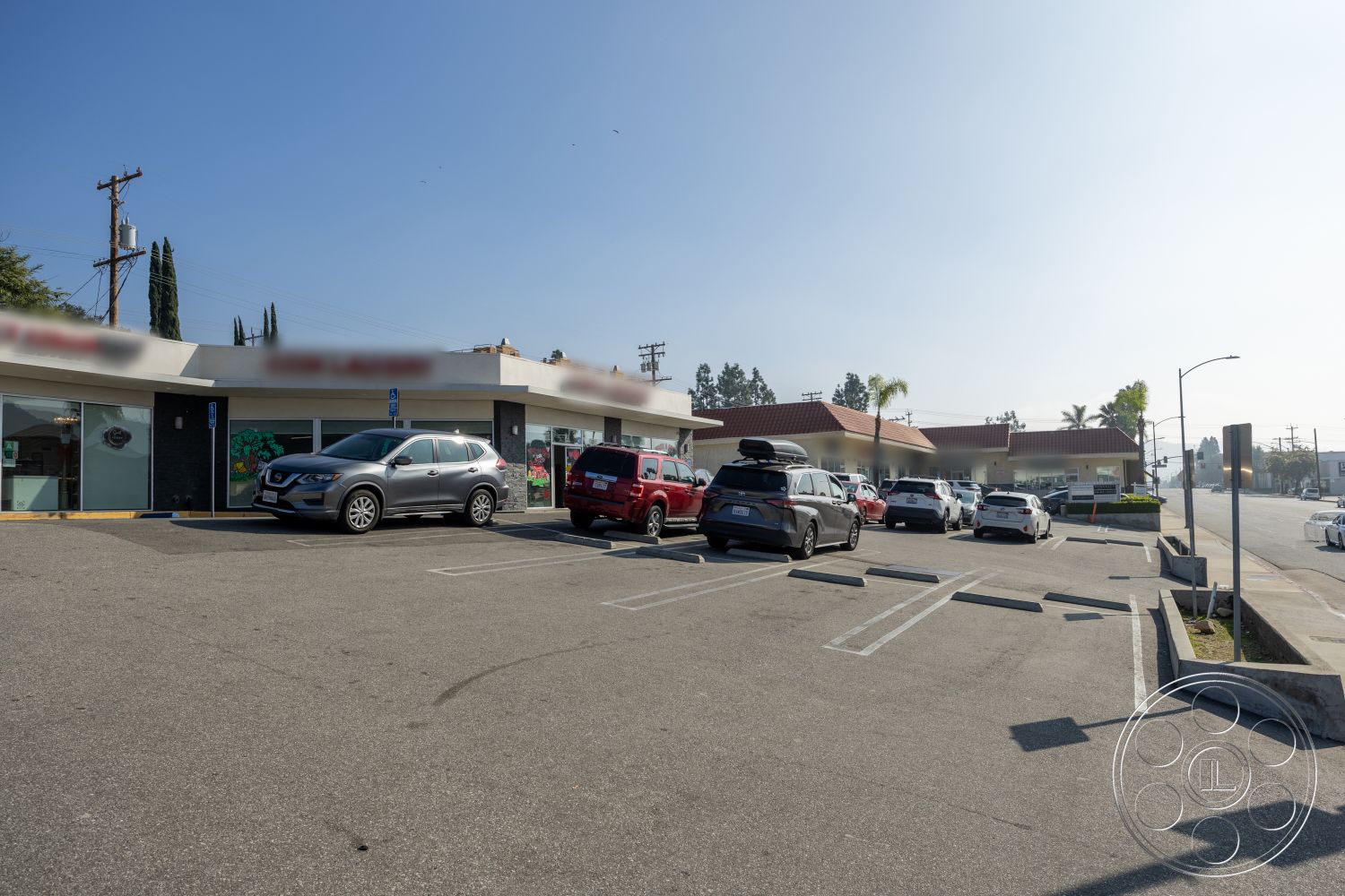 Laundromat 1 - exterior, palm trees, landscaped greenery, urban setting, red tile roof, striped parking spaces, concrete parking lot, accessible parking space, flat roof design, glass storefront windows, commercial building facade, paved access road, single-story retail building, metal pole signage