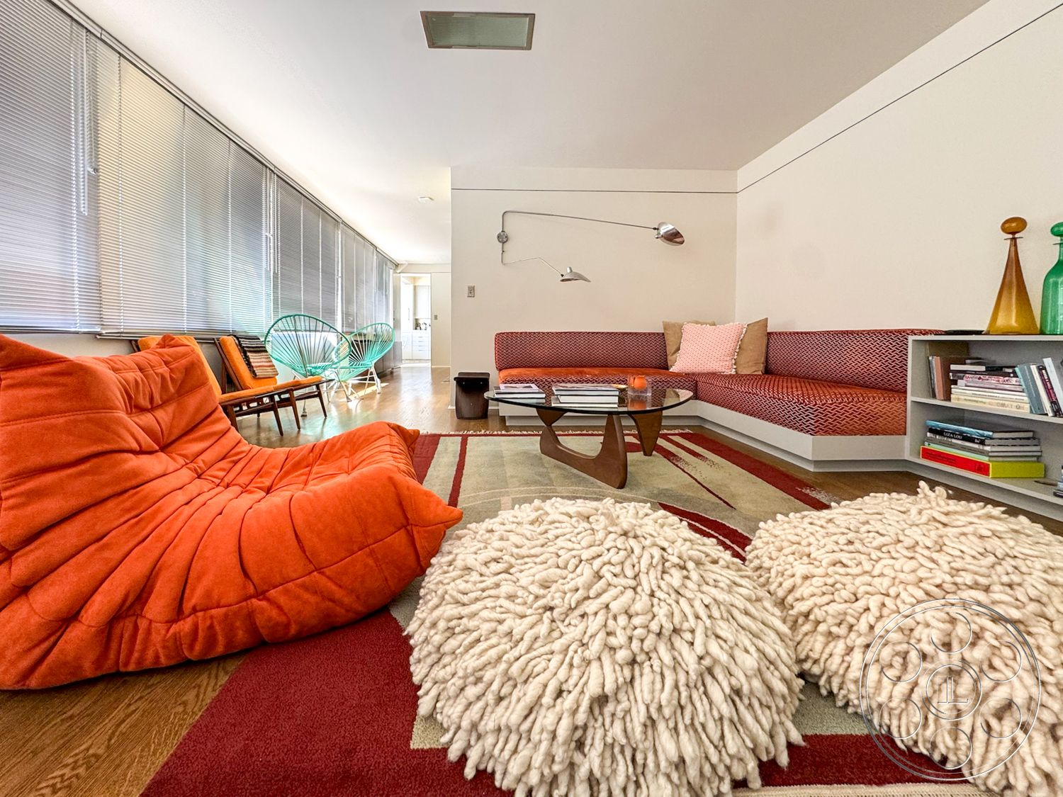 The Kun House - wood flooring, round coffee table, floor-to-ceiling windows, textured throw pillows, modern lounge area, ambient lighting fixture, abstract area rug, orange tufted lounge chair, sectional sofa with patterned upholstery, green wire lounge chairs, contemporary shelving unit