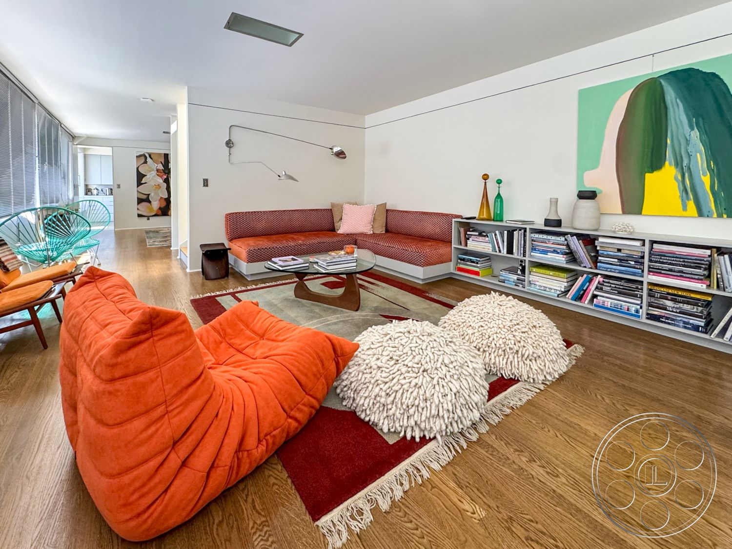 The Kun House - open floor plan, glass coffee table, floor-to-ceiling windows, hardwood living room floors, white painted walls, contemporary art wall hanging, red upholstery sofa, orange bean bag chair, striped textile accent, modern shelving unit, textured throw rug