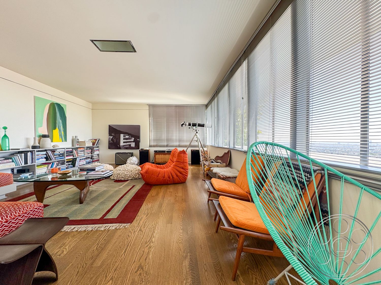 The Kun House - textured area rug, artwork on walls, modern coffee table, exposed ceiling, open living space, mid-century modern design, hardwood living room floors, large windows with horizontal blinds, colorful accent chairs, contemporary shelving unit, functional home office nook