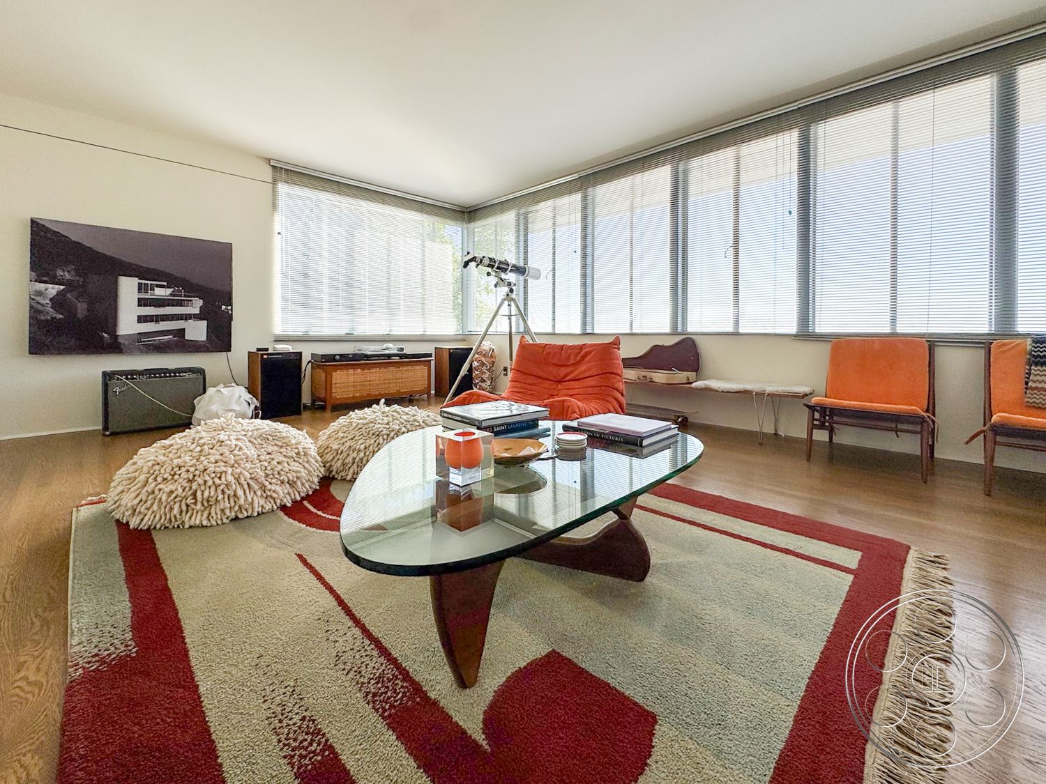 The Kun House - wooden console table, textured area rug, glass coffee table, floor-to-ceiling windows, modernist design elements, hardwood living room floors, open floor plan layout, minimalist wall art, orange upholstered chairs, plush ottomans, industrial ceiling light fixtures