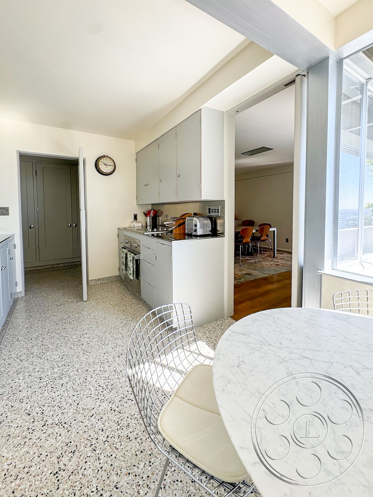 The Kun House - neutral color palette, natural light, minimalist design, floor-to-ceiling windows, arched doorway, marble dining table, stainless steel kitchen appliances, open kitchen layout, functional kitchen workspace, terrazzo kitchen flooring, modern wire dining chair, light gray kitchen cabinets