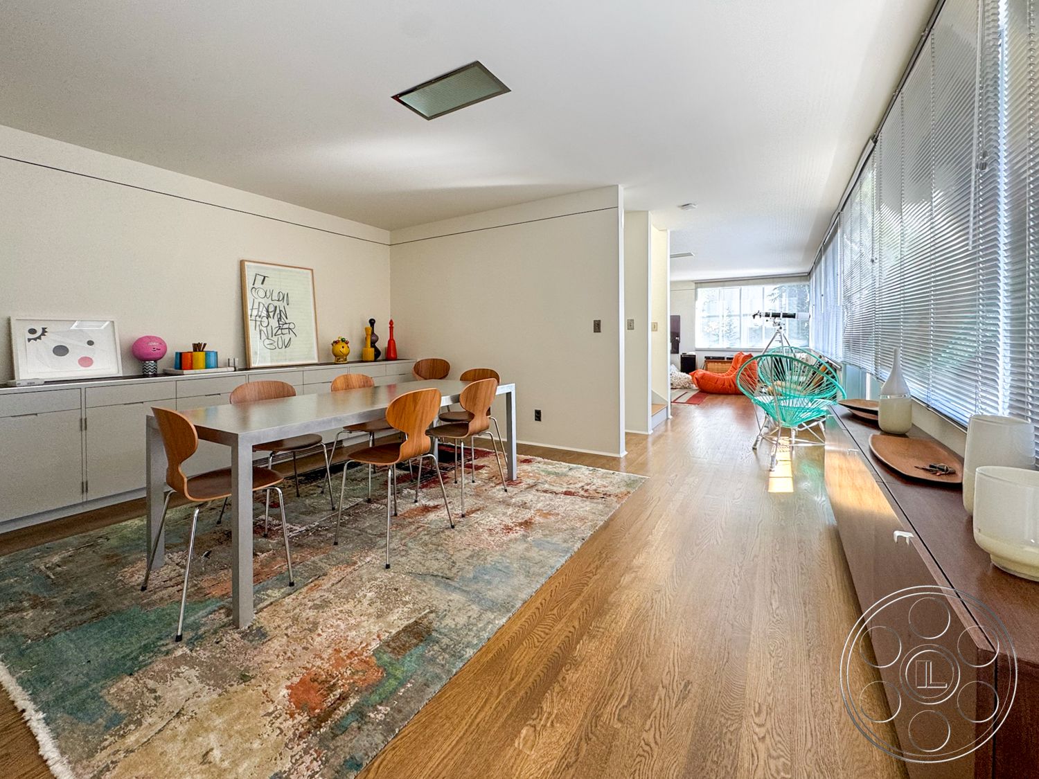 The Kun House - open floor plan, wood dining table, modern art wall decor, light wood floor, contemporary interior, metal dining chairs, natural light-filled space, neutral painted walls, large windows with blinds, colorful accent decor, area rug with abstract pattern, built-in storage unit, decorative vases on sideboard