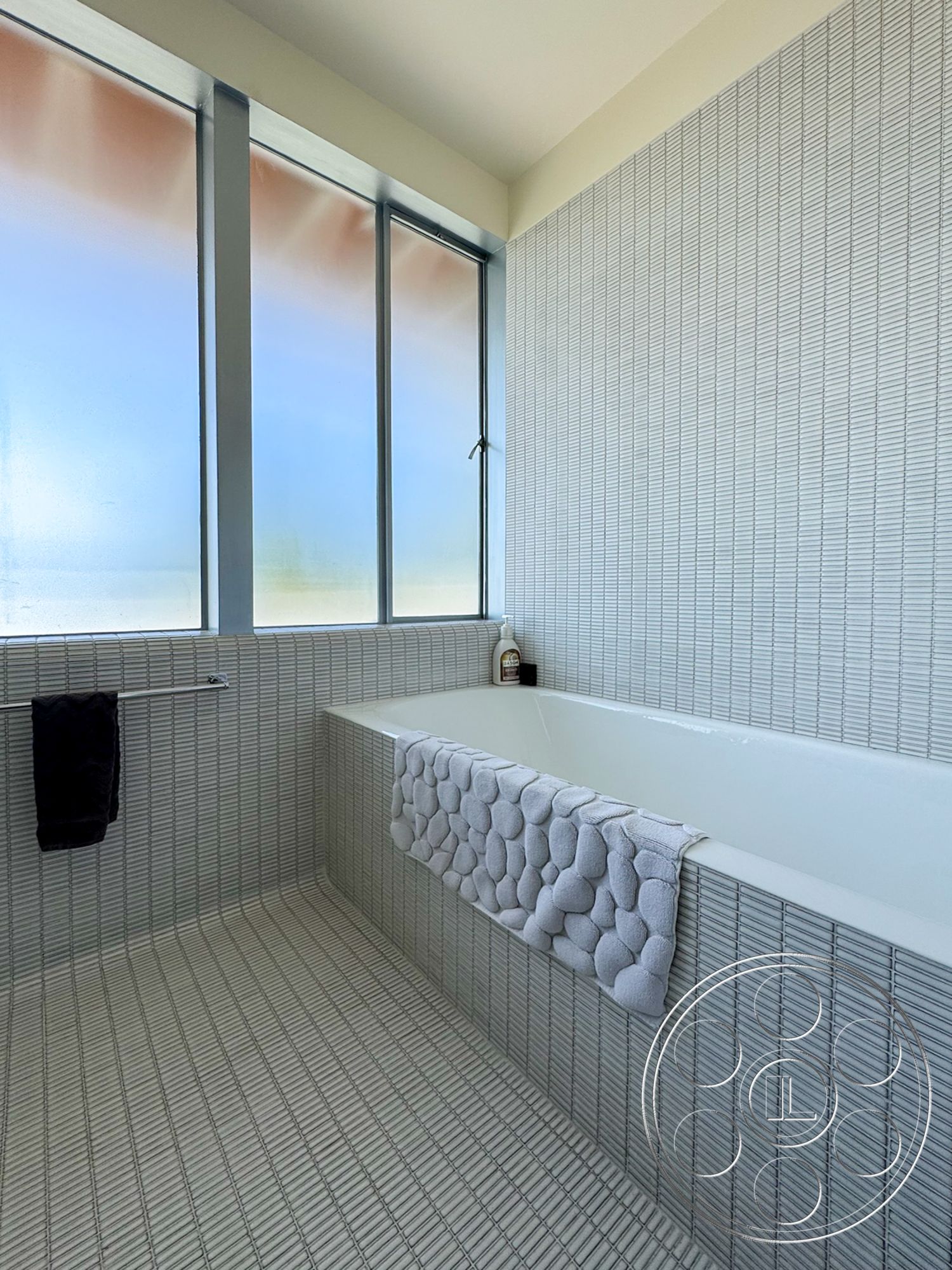 The Kun House - minimalist decor, neutral color palette, modern aesthetic, contemporary bathroom design, rectangular bathtub, textured tile bathroom walls, square tile bathroom flooring, framed frosted glass windows, floating towel rack, soft textured bath mat, linear tile pattern