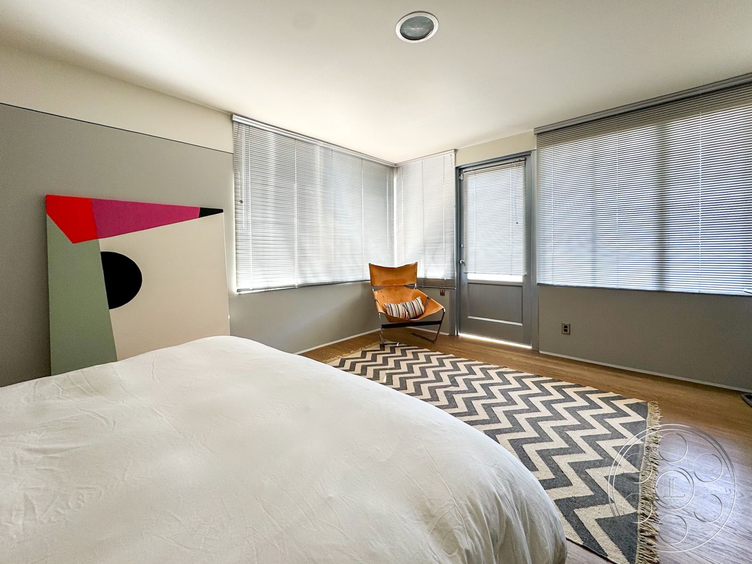 The Kun House - neutral color palette, natural light, minimalist design, modern art wall decor, wooden armchair, painted walls, hardwood bedroom floors, large windows with blinds, zigzag area rug