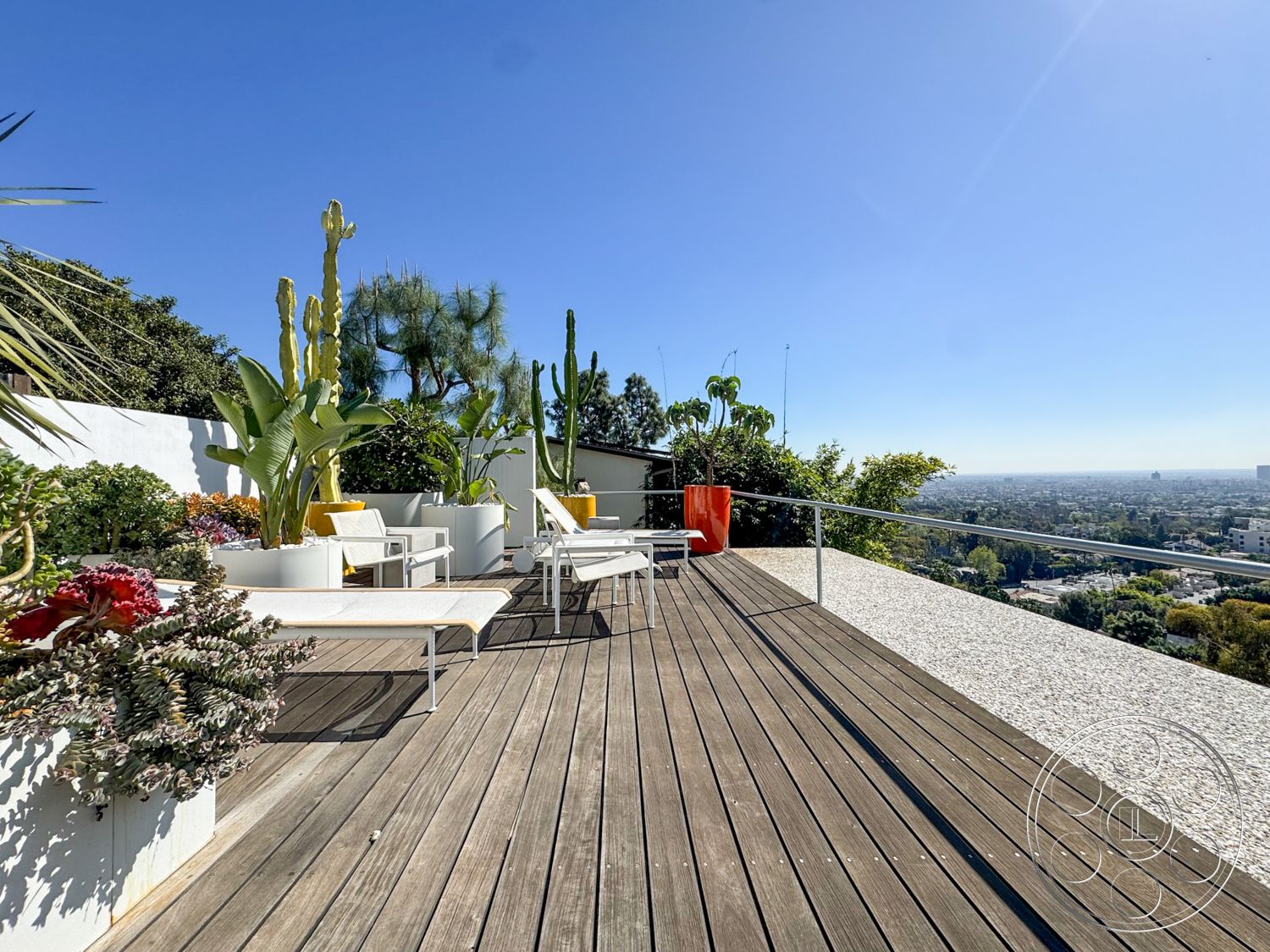 The Kun House - exterior, outdoor living space, clear glass railing, tropical landscaping, sunny terrace, modern lounge chairs, mountain view setting, concrete planter boxes, painted accent wall, wooden patio decking, low-profile succulents, tall potted cacti