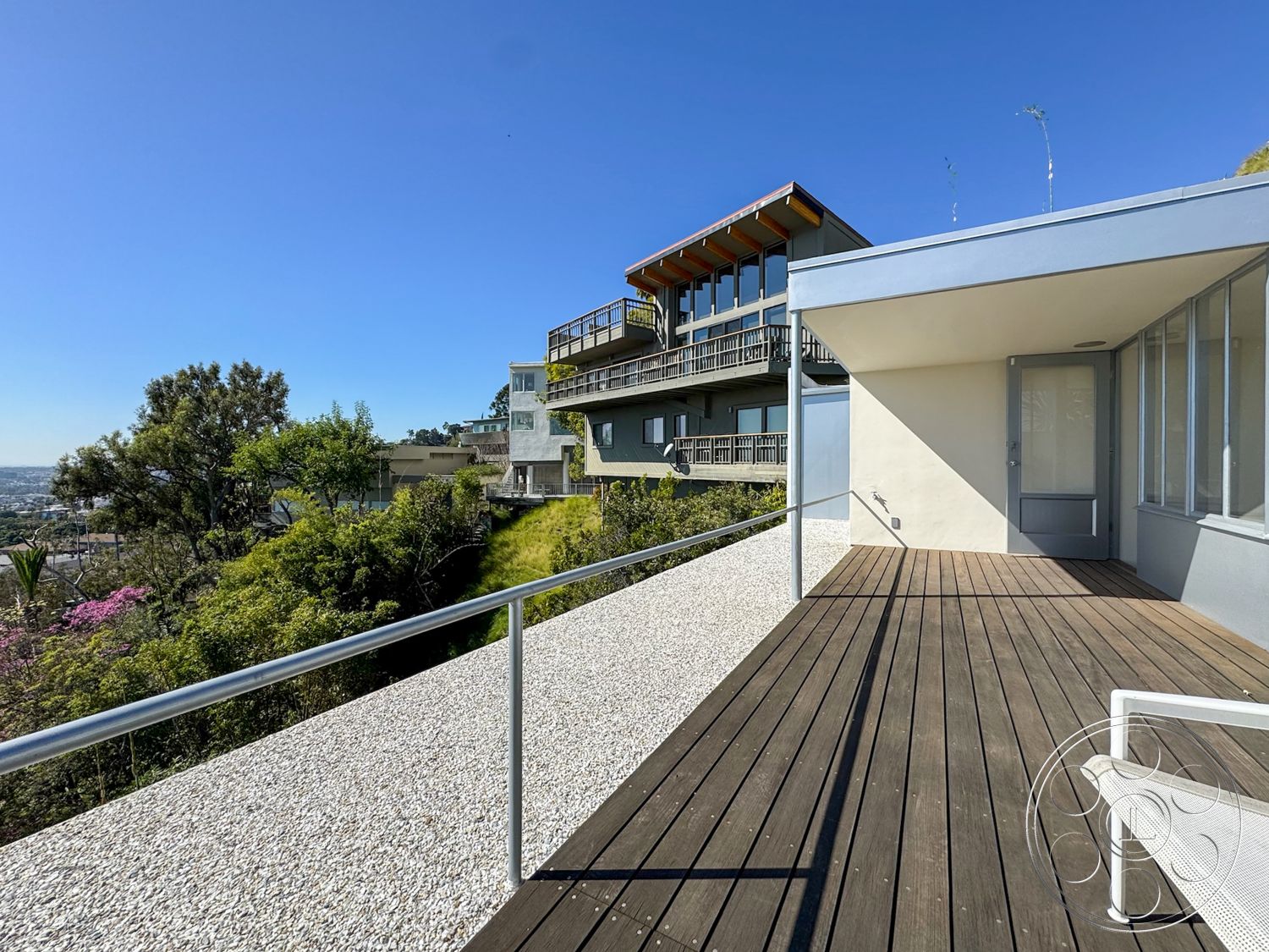 The Kun House - exterior, large glass windows, steel railing, open outdoor space, concrete elements, city skyline view, flat roof design, natural light exposure, wood deck flooring, gravel patio, two-story modern house, green hillside landscape