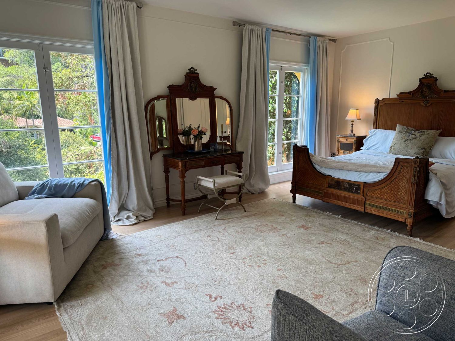 Medit 156 - textured area rug, woven chair, floor-to-ceiling windows, white bedding, floral decor, blue accent pillows, natural greenery view, soft lighting fixtures, light-colored curtains, hardwood bedroom floors, cream-painted walls, Crown molding details, traditional style bed, wooden decorative mirror, neutral-tone sofa