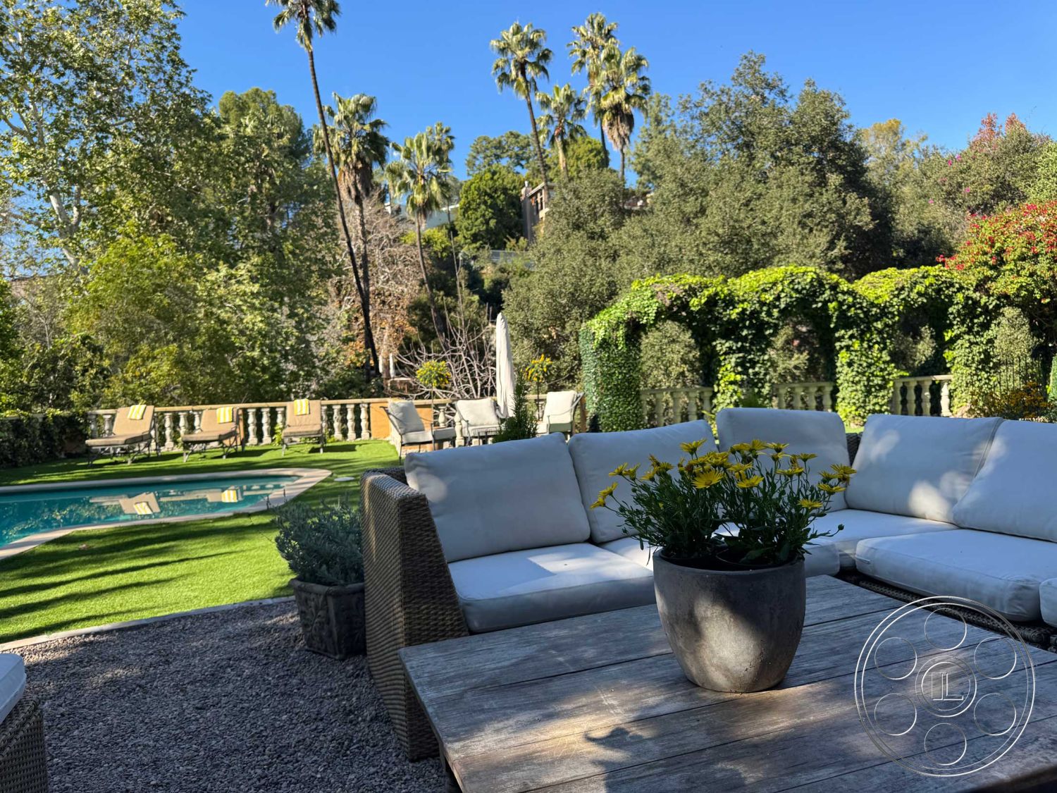 Medit 156 - exterior, palm trees, woven outdoor furniture, in-ground swimming pool, rectangular pool, lush green landscaping, sunny outdoor setting, gravel patio flooring, wooden outdoor dining table, artificial grass lawn, stone flower pot, covered lounging area, climbing ivy on trellis