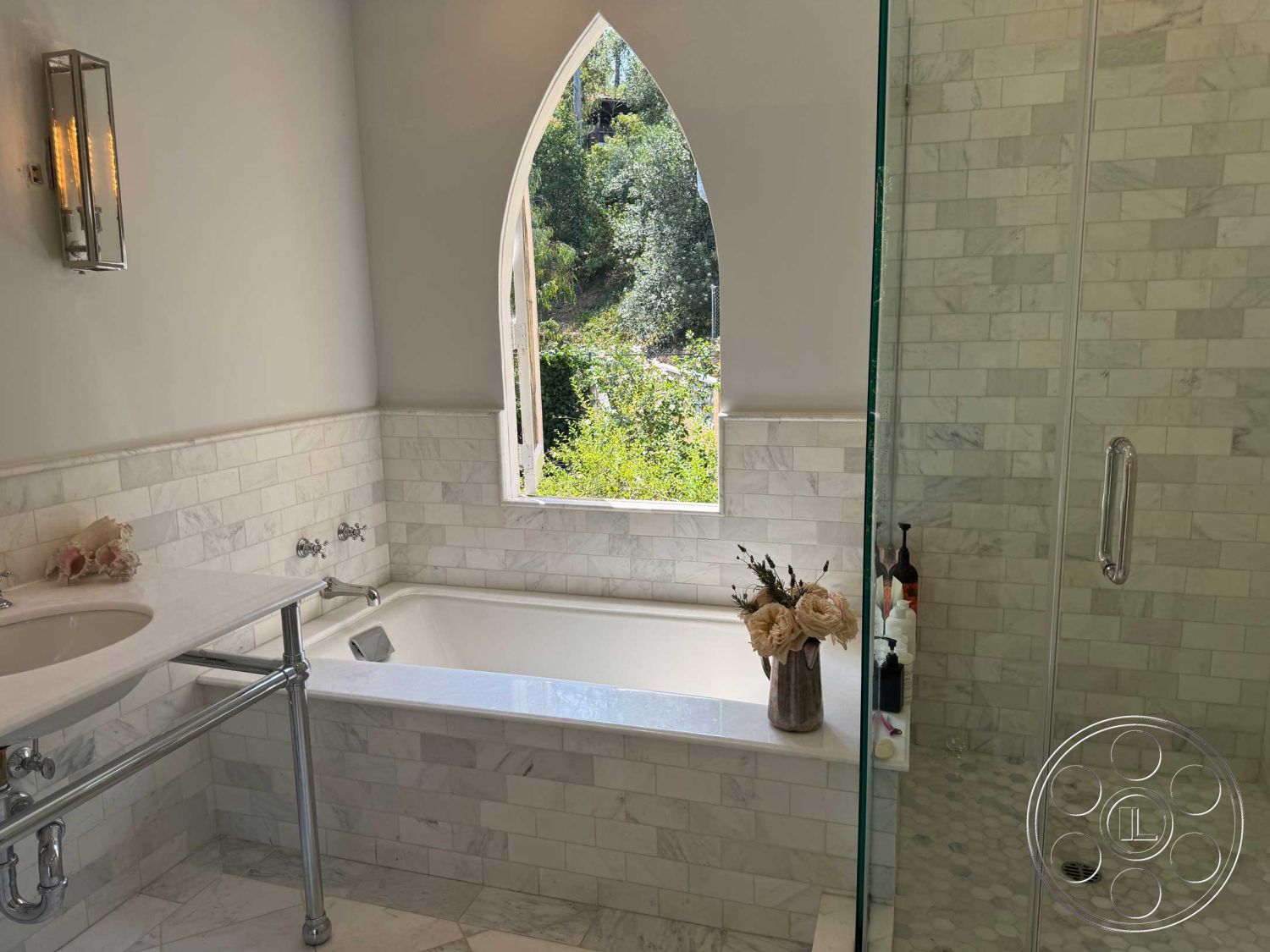 Medit 156 - glass shower enclosure, chrome plumbing fixtures, natural greenery view, arched window, textured plaster wall, neutral painted walls, marble bathroom walls, marble countertop sink, wall-mounted lighting fixtures, marble bathtub surround, hexagonal marble shower floor tiles