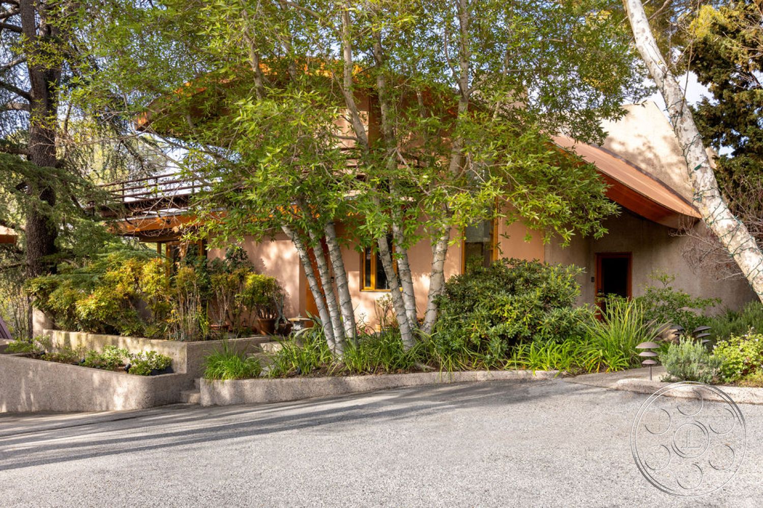 Mid-Century Exotic - exterior, paved driveway, stucco walls, natural stone pathways, wooden window frames, landscaped garden area, rustic architectural style, tree canopy shading, metal roof overhang, concrete garden planters, various shrubs and foliage, organic shape design, modern harmony with nature