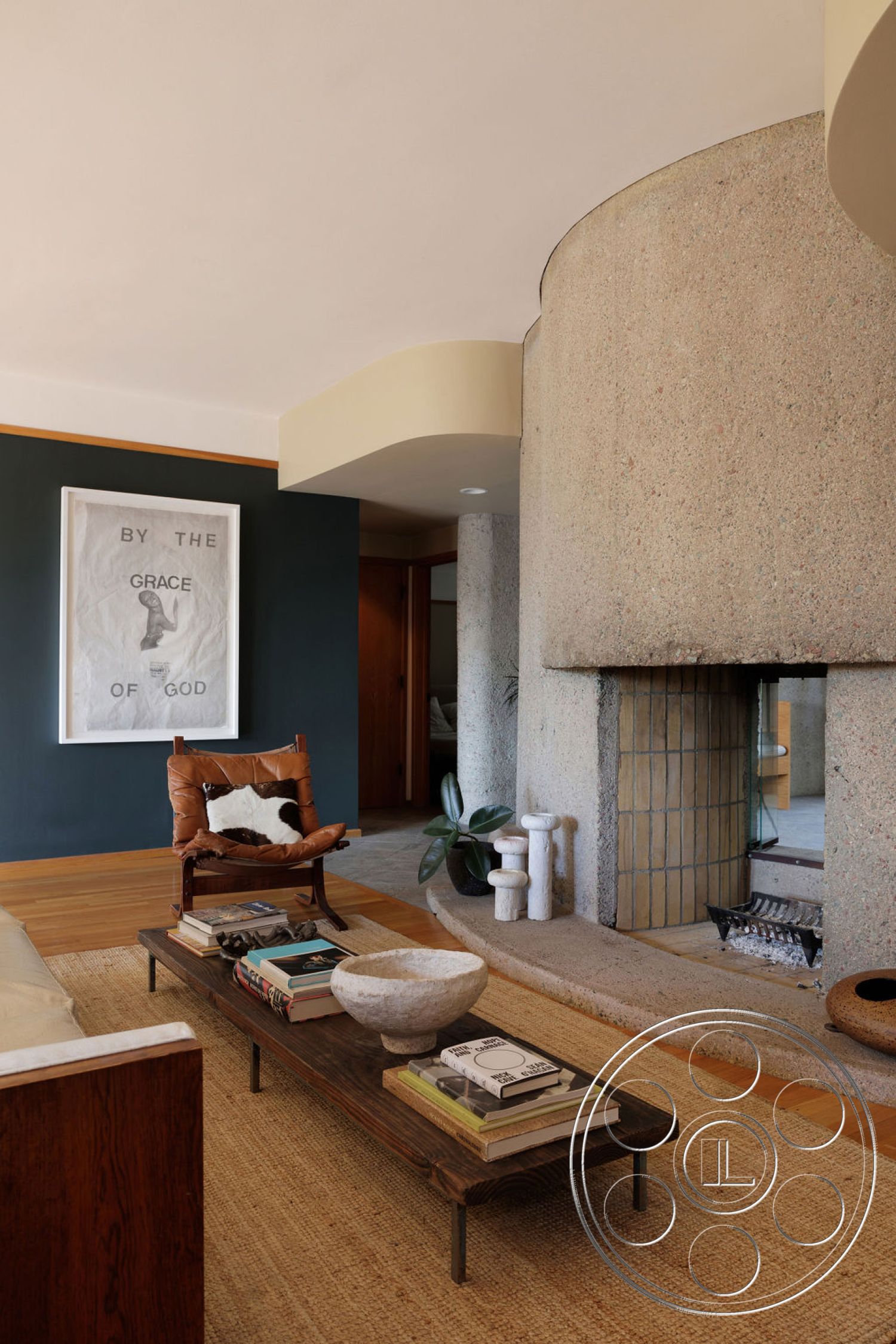 Mid-Century Exotic - neutral color palette, wooden coffee table, minimalist design elements, modern art decor, framed art on wall, natural plant decoration, exposed aggregate concrete fireplace surround, curved concrete architectural details, hardwood floor finish, earthy jute area rug, tan leather accent chair
