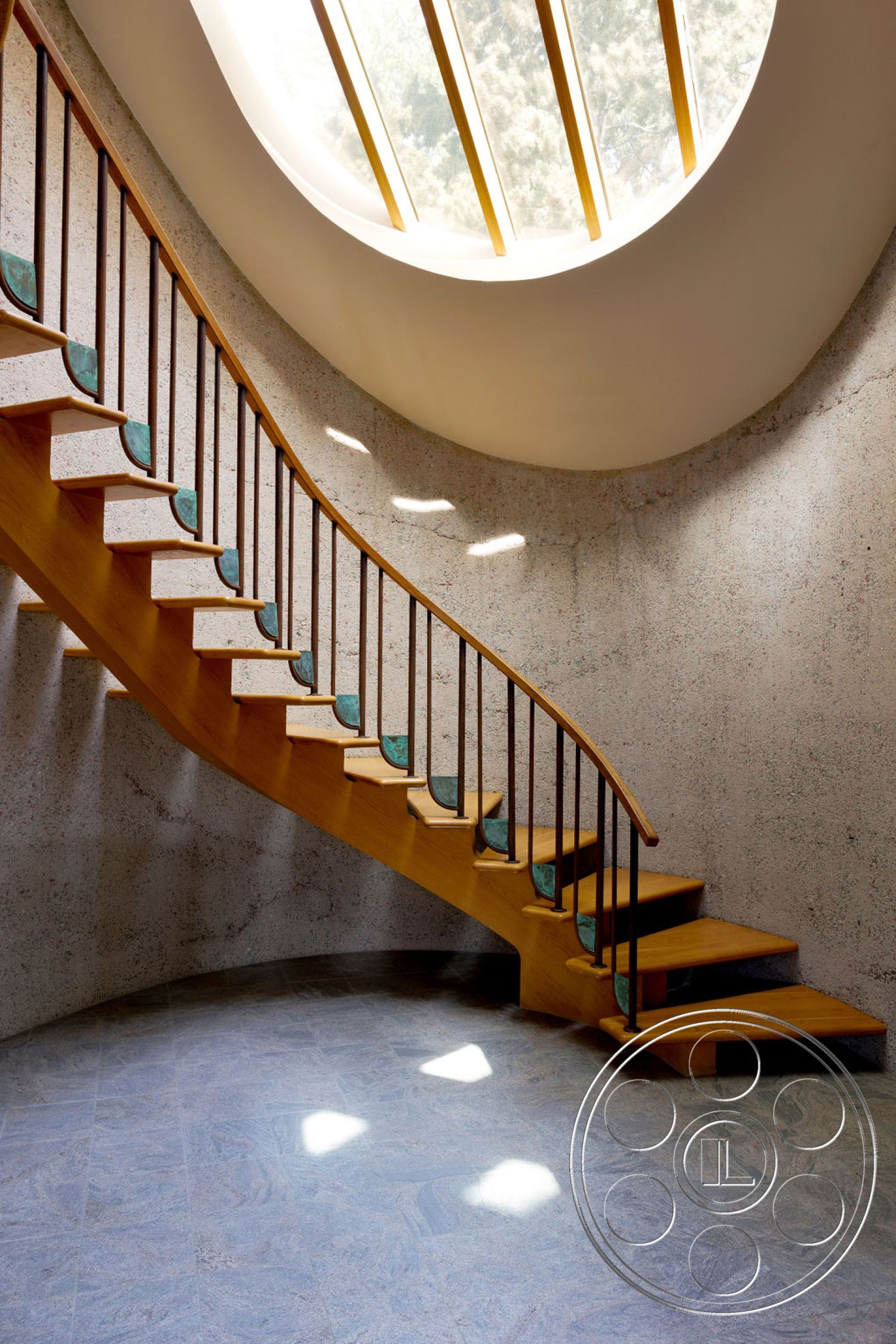 Mid-Century Exotic - textured concrete walls, smooth stone flooring, curved staircase, steel stair railings, vaulted ceiling with skylight, open wooden staircase, light wood treads, blue-green stair risers, natural light beams