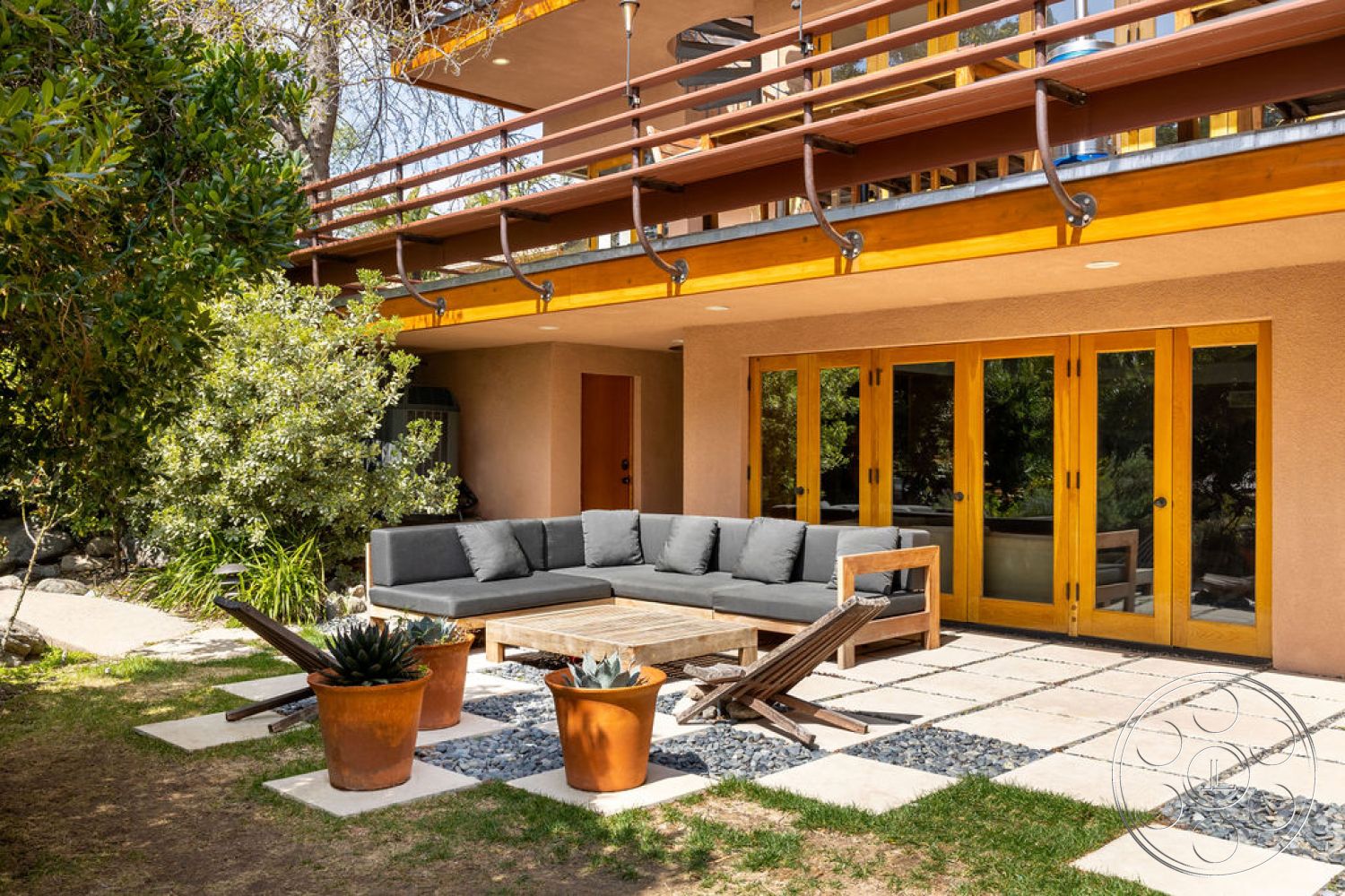 Mid-Century Exotic - exterior, potted plants, glass sliding doors, suburban backyard, rustic wood coffee table, two-story home, exposed wood ceiling beams, landscaped garden area, concrete patio flooring, wood deck railing, open outdoor living space, built-in outdoor seating, paver stones with gravel border, modern outdoor sofa