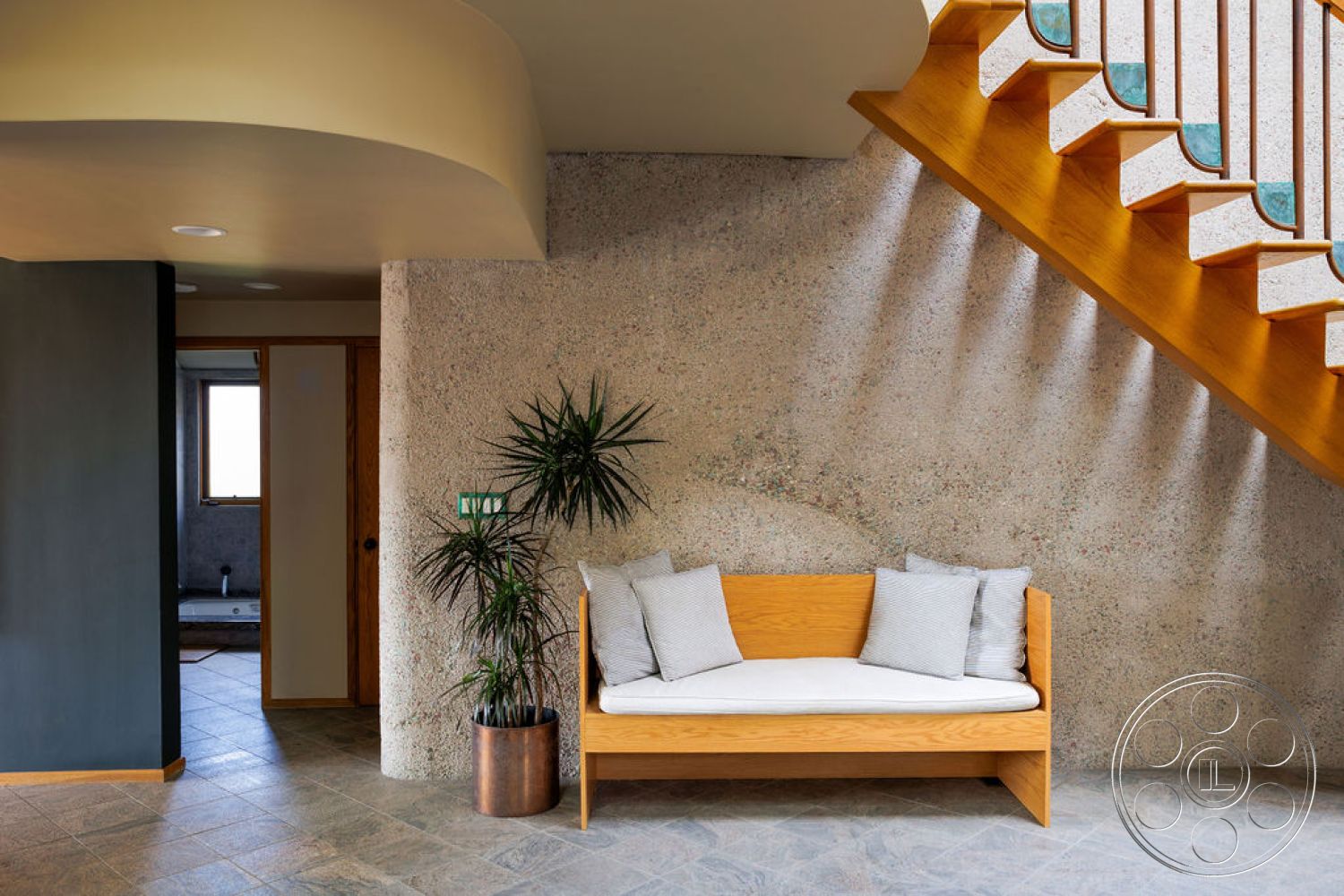 Mid-Century Exotic - open floor plan, entryway, soft ambient lighting, curved ceiling, stone tile flooring, exposed aggregate wall, wooden stair railings, light gray throw pillows, natural wood bench with white cushion, indoor plant in metallic planter