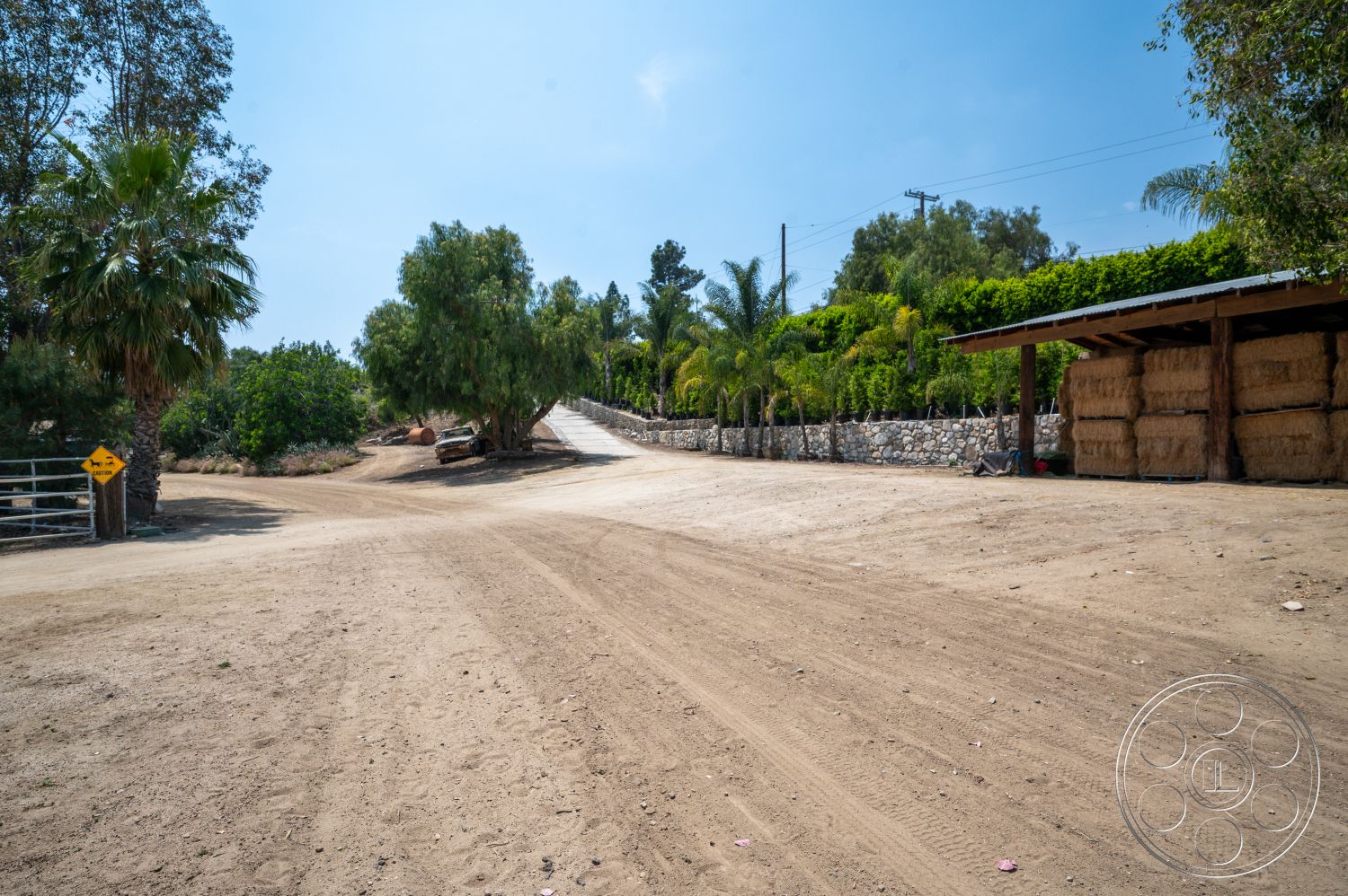 Ranch 6 - exterior, palm trees, stone wall, tropical landscaping, rural setting, deciduous trees, sunny outdoor environment, hay bales, dirt road driveway, outdoor agricultural storage
