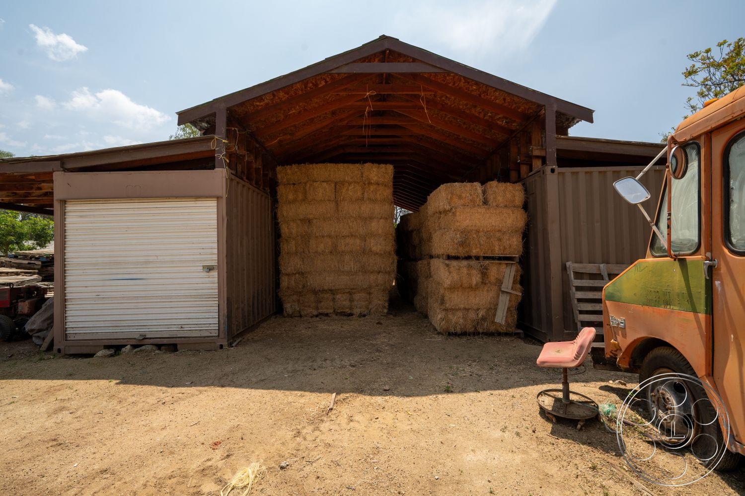 Ranch 6 - exterior, rustic architecture, agricultural setting, wood beam ceiling, dirt ground surface, metal storage container, straw bale storage, rolling steel door, shed structure, open-sided barn