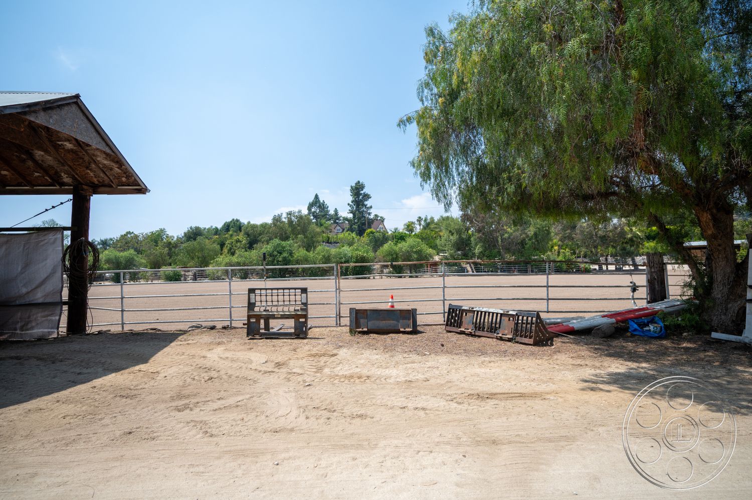 Ranch 6 - exterior, mature trees, metal roof, landscape greenery, sunlit environment, open field setting, wooden barn structure, outdoor storage area, dirt riding arena, fence enclosure, outdoor horse area