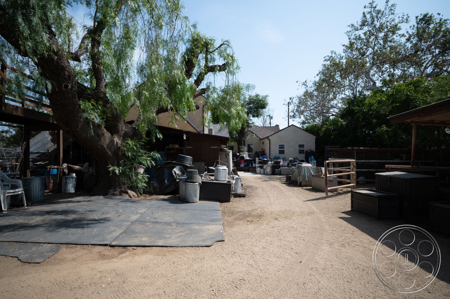 Ranch 6 - exterior, gravel driveway, large shade tree, open backyard space, concrete outdoor flooring, metal storage containers, weathered wood deck, brown clapboard house, bark mulch landscaping, fencing around yard