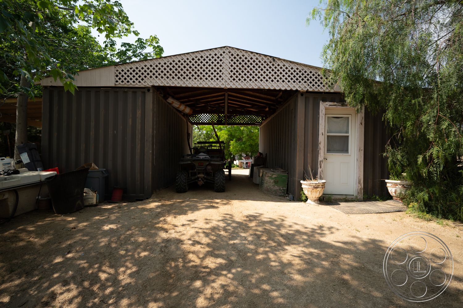 Ranch 6 - exterior, natural landscaping, surrounding trees, rustic aesthetic, rural setting, gravel driveway, metal siding, wood lattice roof structure, open-air storage area, single door entrance