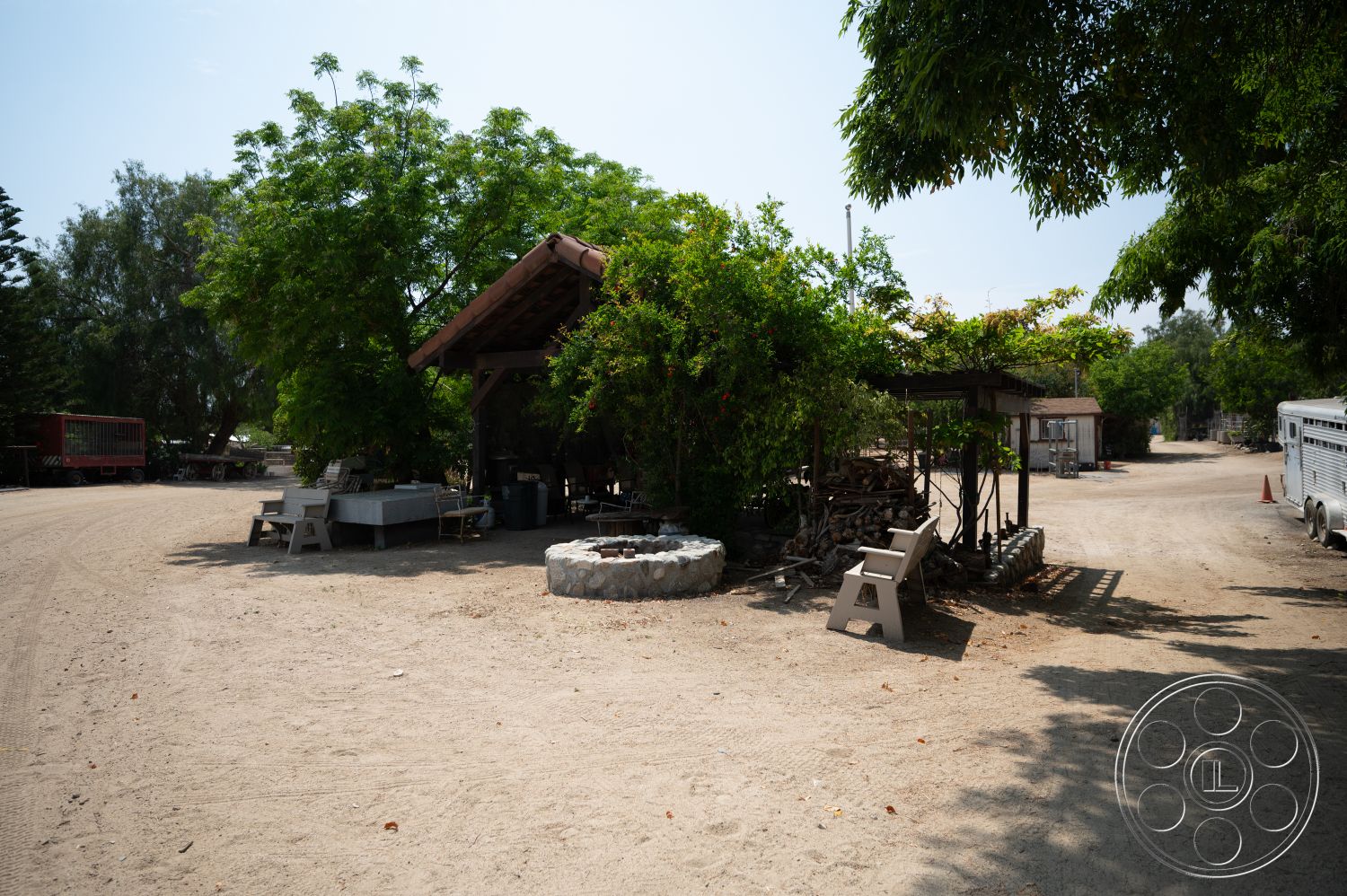 Ranch 6 - exterior, dirt pathway, rustic outdoor setting, natural stone fire pit, wooden support beams, concrete bench seating, landscaped outdoor space, outdoor gathering area, wooden roof with overhang, surrounding lush green trees